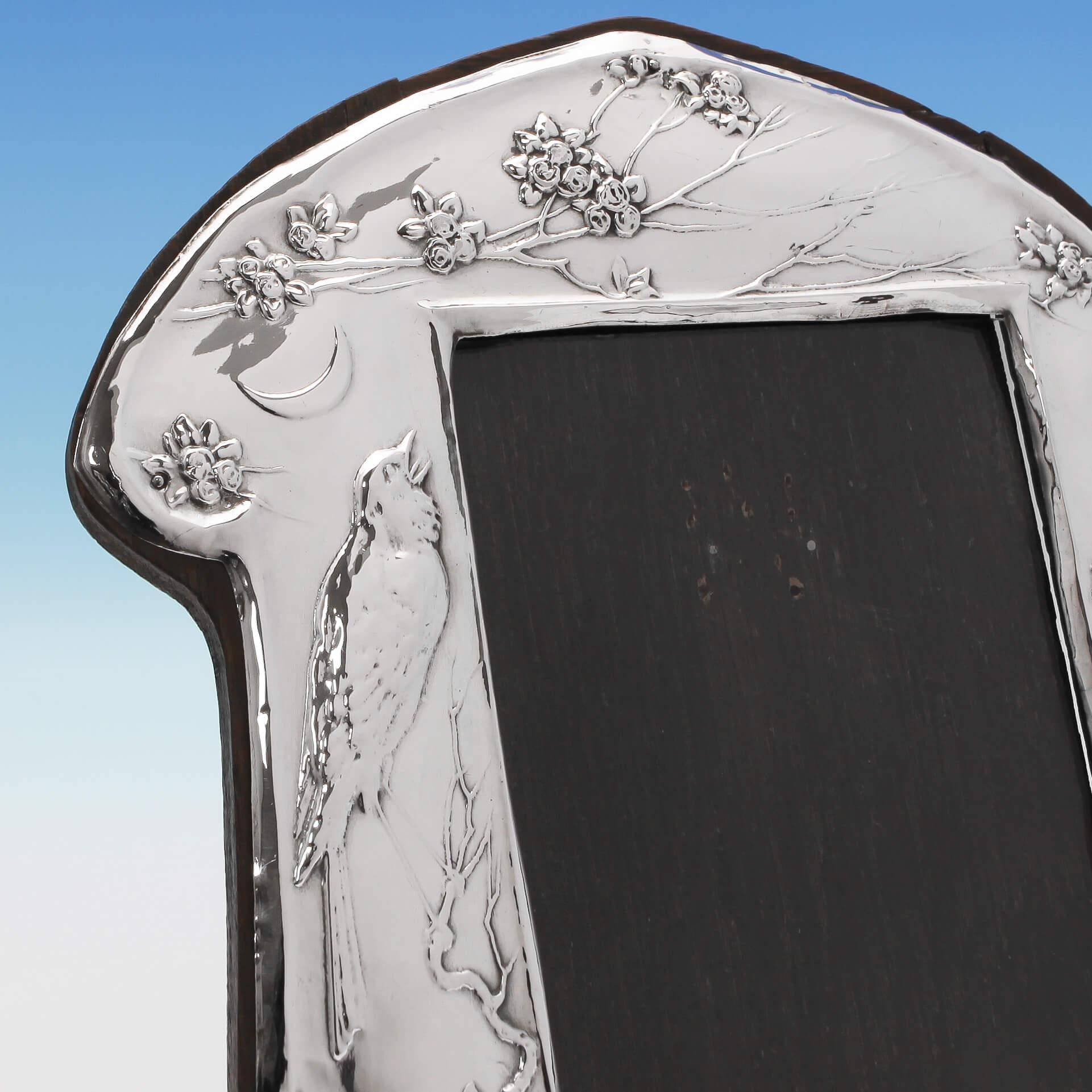 Hallmarked in Birmingham in 1911, this pretty, antique, George V, sterling silver, photograph frame features Art Nouveau decoration depicting a song bird and floral scroll. The shaped frame stands on a wooden easel back, and measures 7