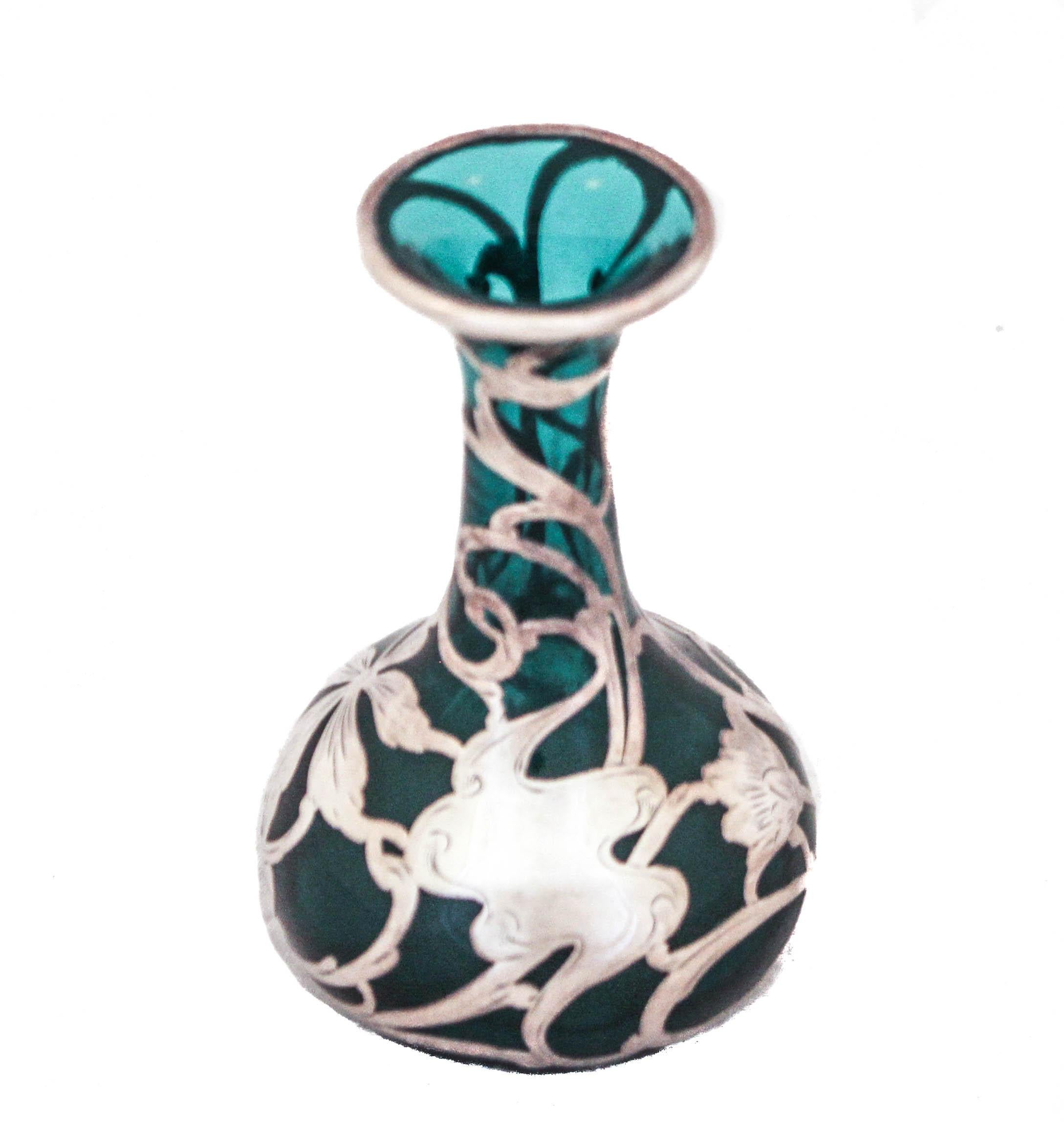 Being offered is a sterling silver Art Nouveau overlay vase in a teal color.  The silver Art Nouveau design is wraps around the entire vase with swirls, flowers and leaves — all motifs in that genre.  What’s very special is that unlike most overlay