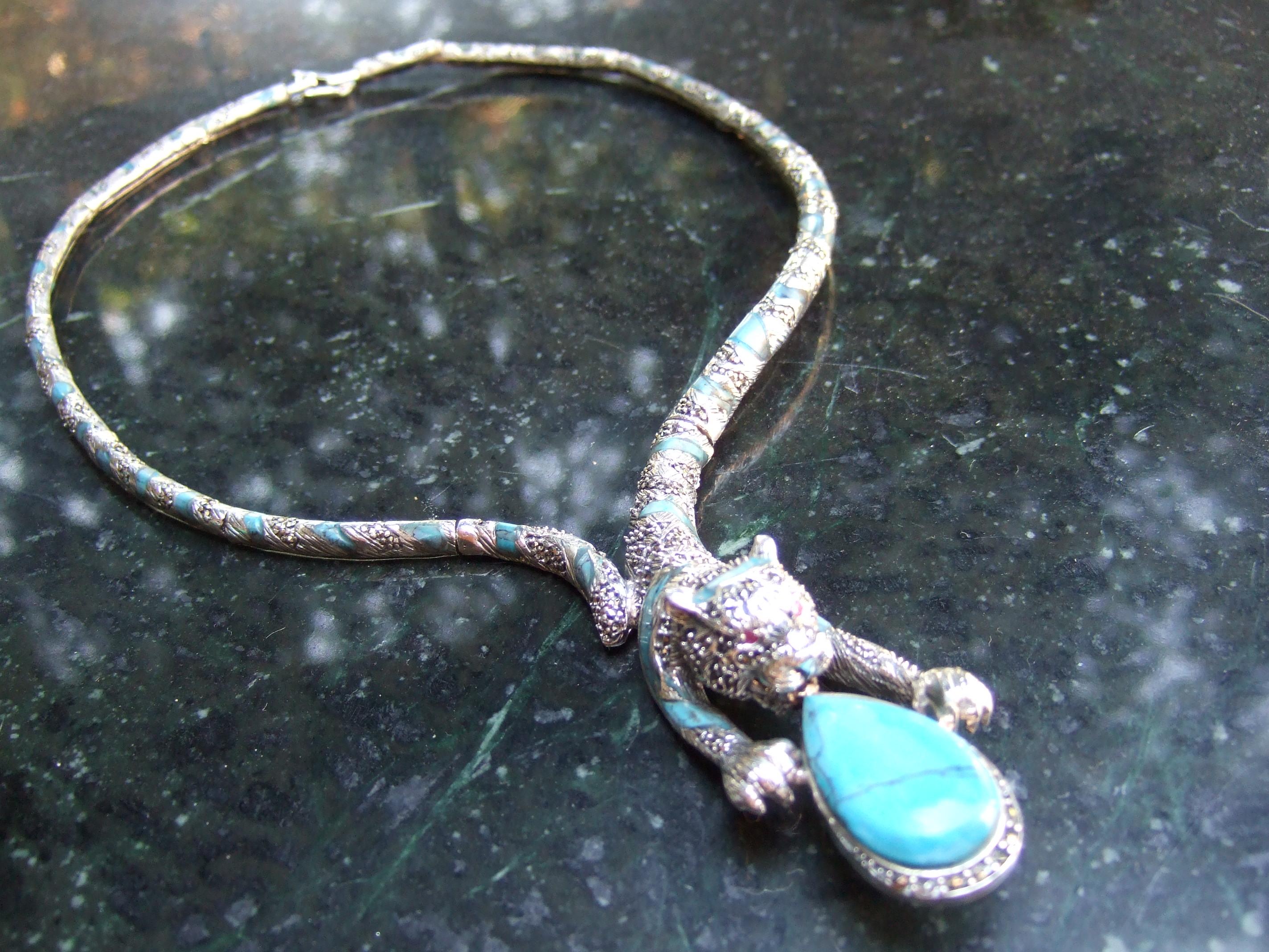 Exotic sterling silver articulated enamel tiger choker necklace 21st c 
The artisan choker necklace is designed with a sleek feline figure with tiny gazing garnet eyes 
The panther is clutching a tear dropped shaped smooth turquoise stone 

The