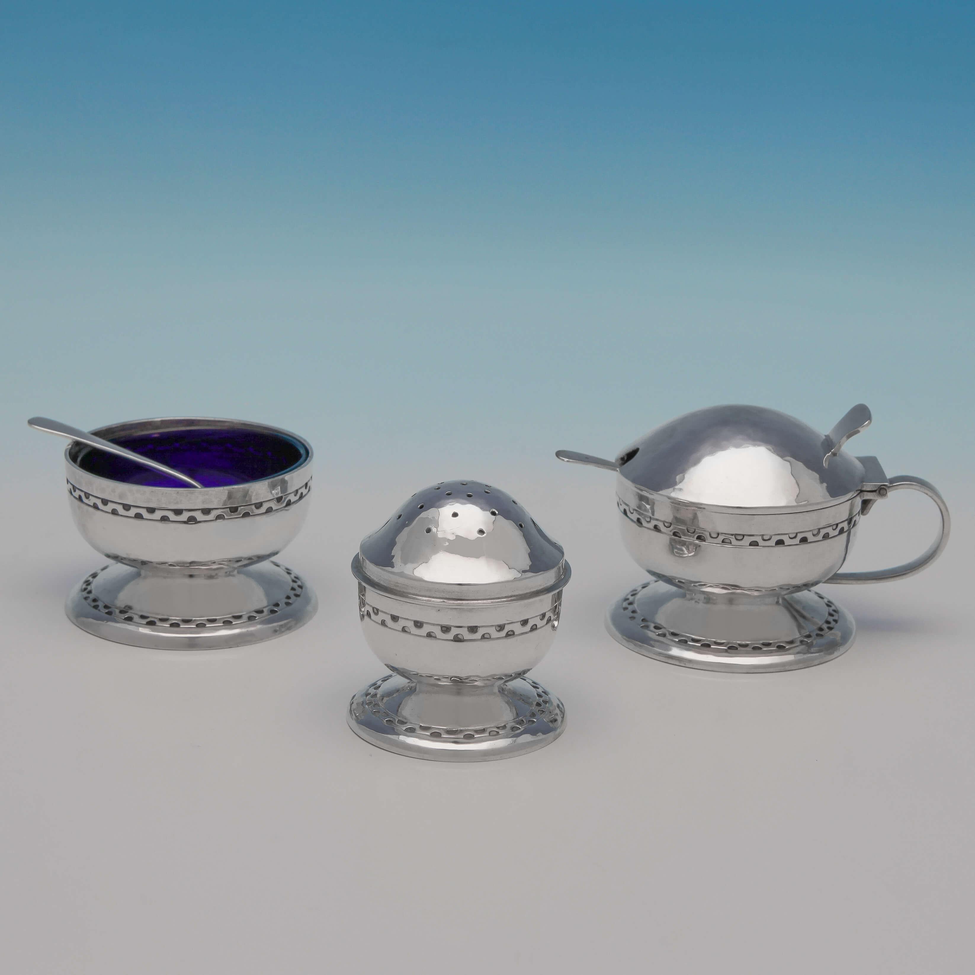 Hallmarked in Birmingham, in 1939, by Liberty & Co., this fantastic and collectible sterling silver Arts & Crafts condiment set has the typical features of the period, with hand-hammered bodies and pattern detailed borders. The original spoons are