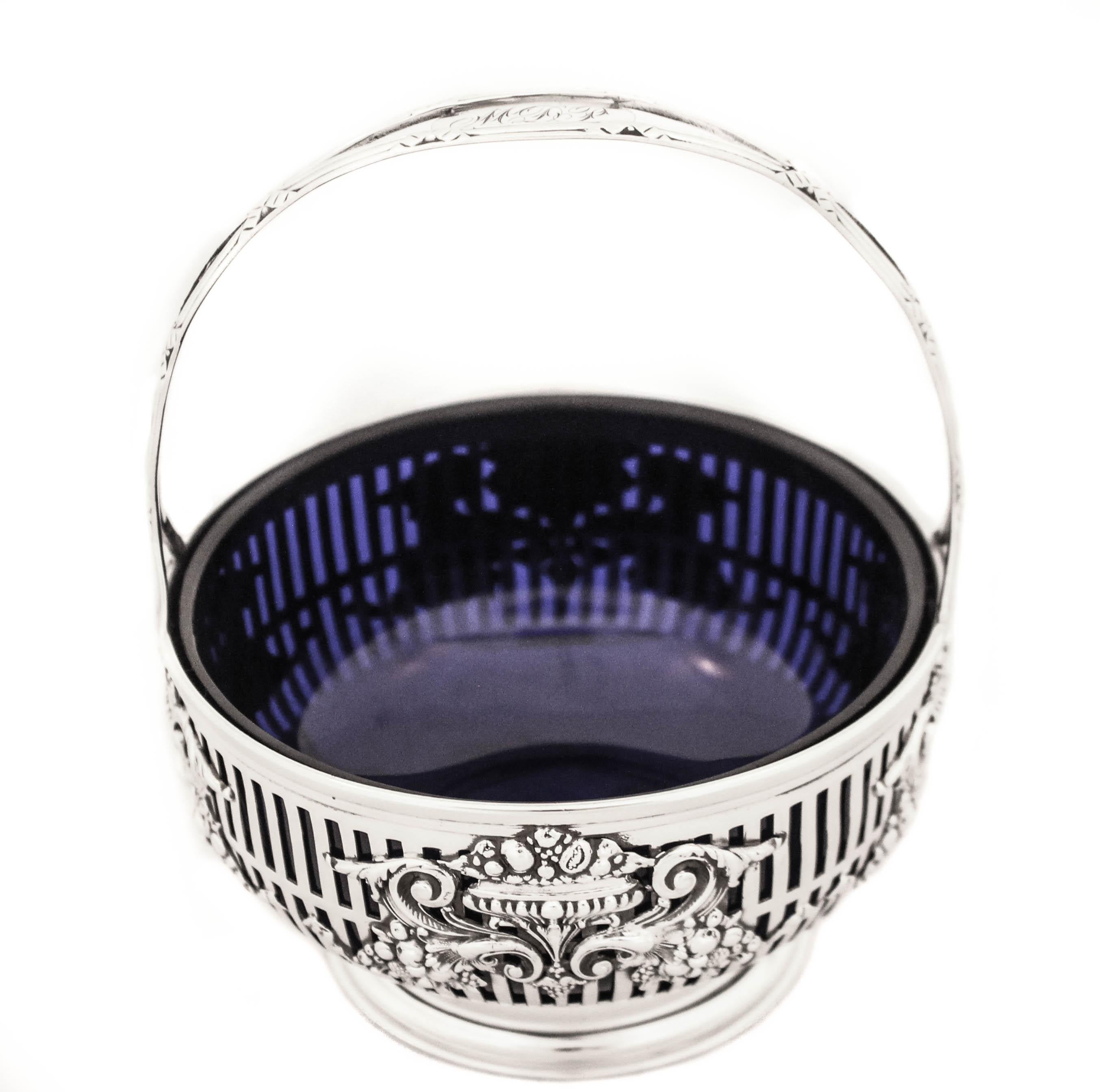 We are delighted to offer you this sterling silver basket with a cobalt blue liner. An elaborate pattern of clustered fruit and flowers decorate the sides of the basket. The cobalt glass pops through the cutout design. The handle is stationary and