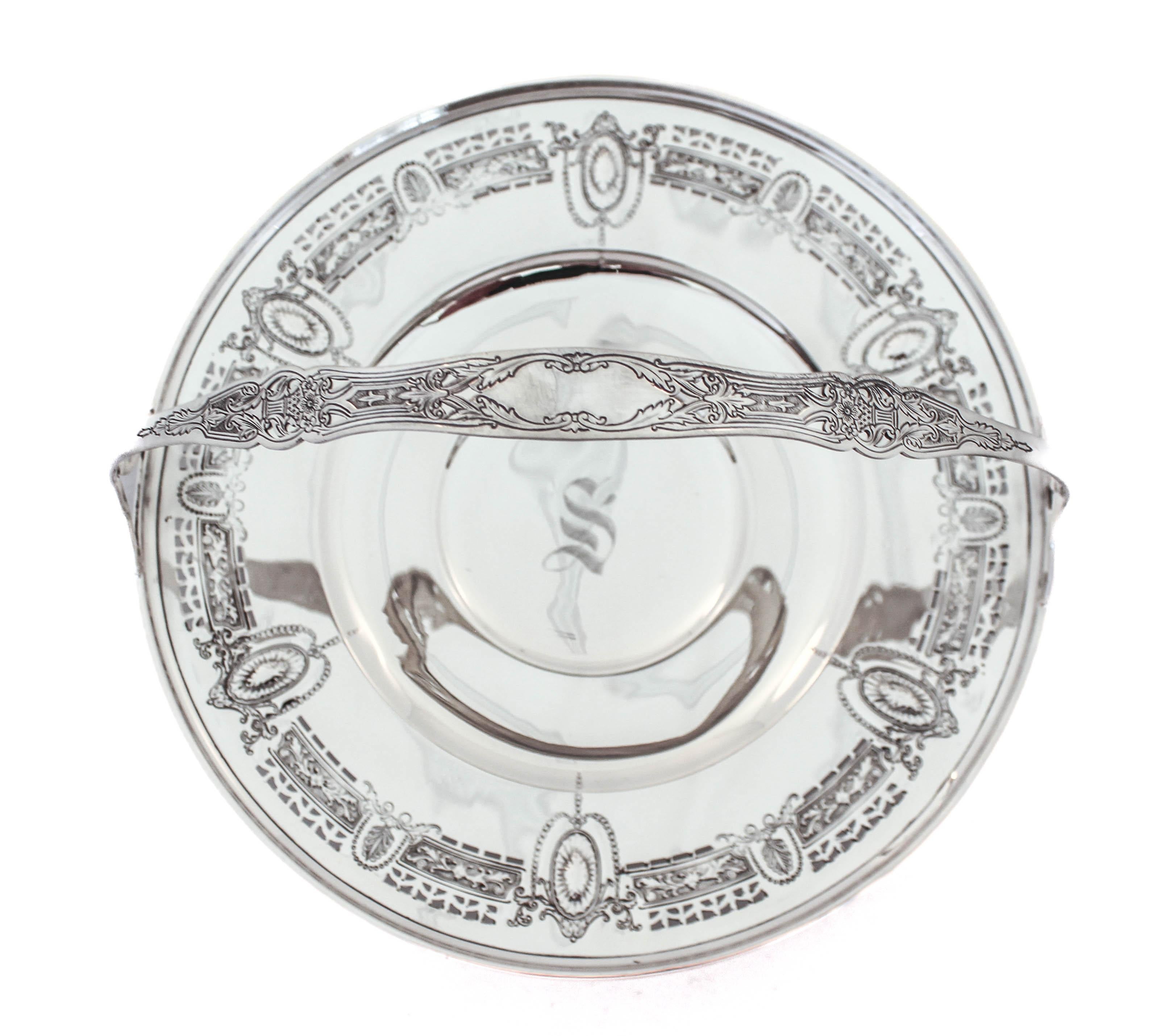 Being offered is a sterling silver basket.  The plate has medallions interspersed with reticulated cutouts.  Old world elegance all around the edge.  The handle has an etched design of floral bouquets and in the center a cartouche— a space for your
