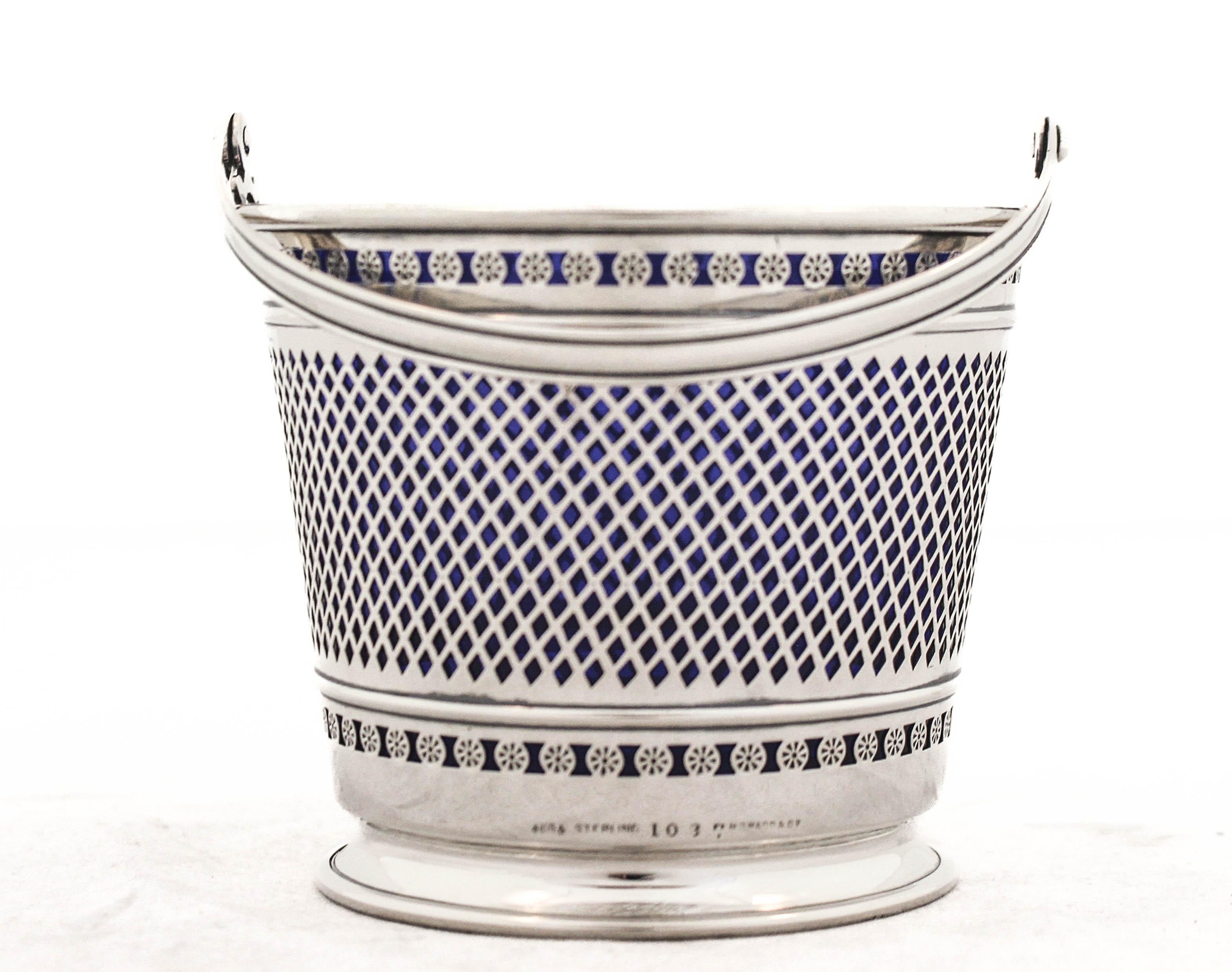 Being offered is a sterling silver basket with the original cobalt liner by George Henckel Silver of New York. The silver basket has two reticulated patterns; in the center a checkered design and on top and bottom a floral design.  The handle folds