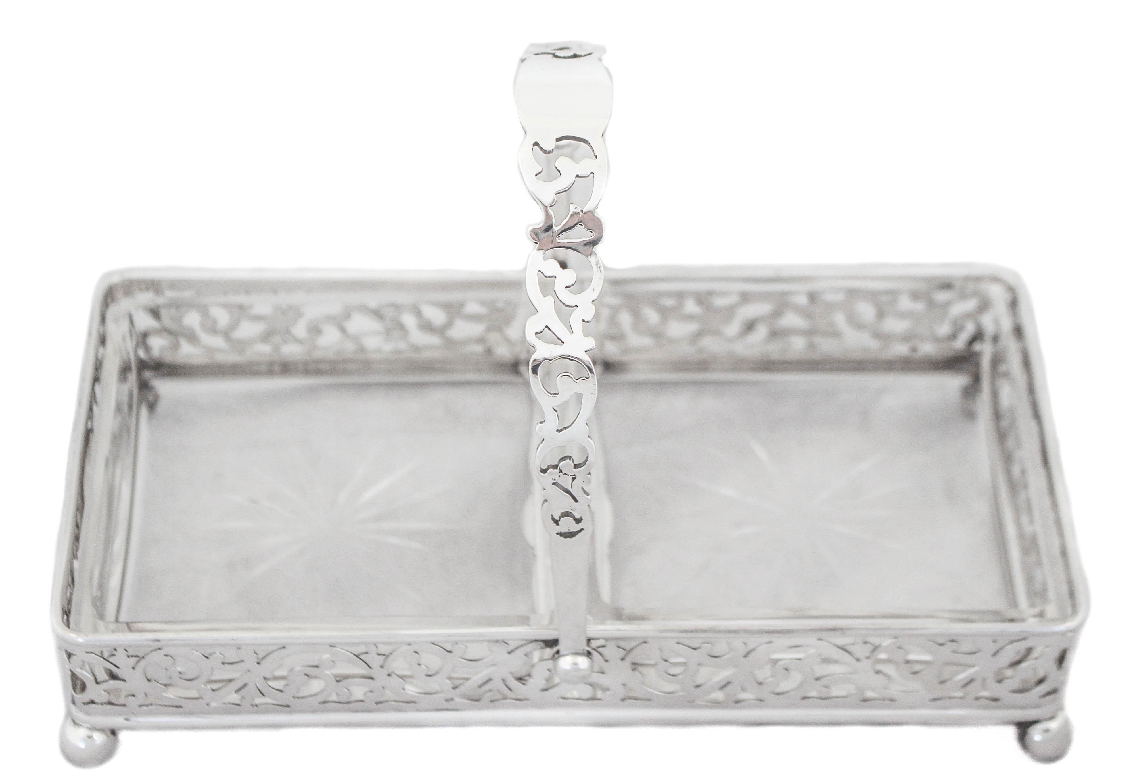 Being offered is a sterling silver basket with two square crystal sectionals. The body and handle have a lattice pattern that allows the glass to show through. Standing on four balls the basket is propped off the surface. The handle folds down for