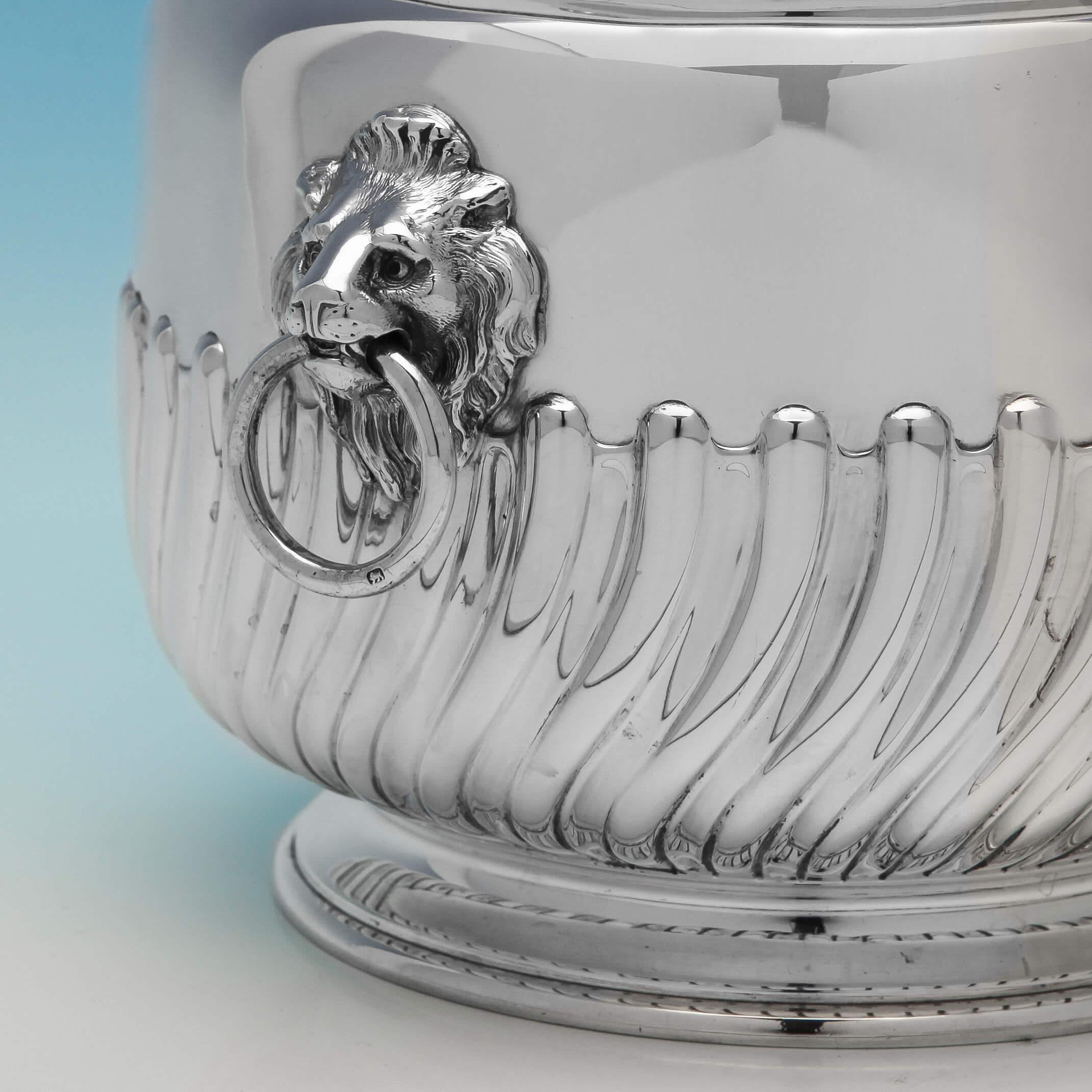 Hallmarked in London in 1889 by Barnards, this attractive Victorian, antique, sterling silver biscuit box, has swirled and sunken half fluting, in the Queen Anne style. It has a flush hinged lid and applied lion mask drop ring handles. This biscuit