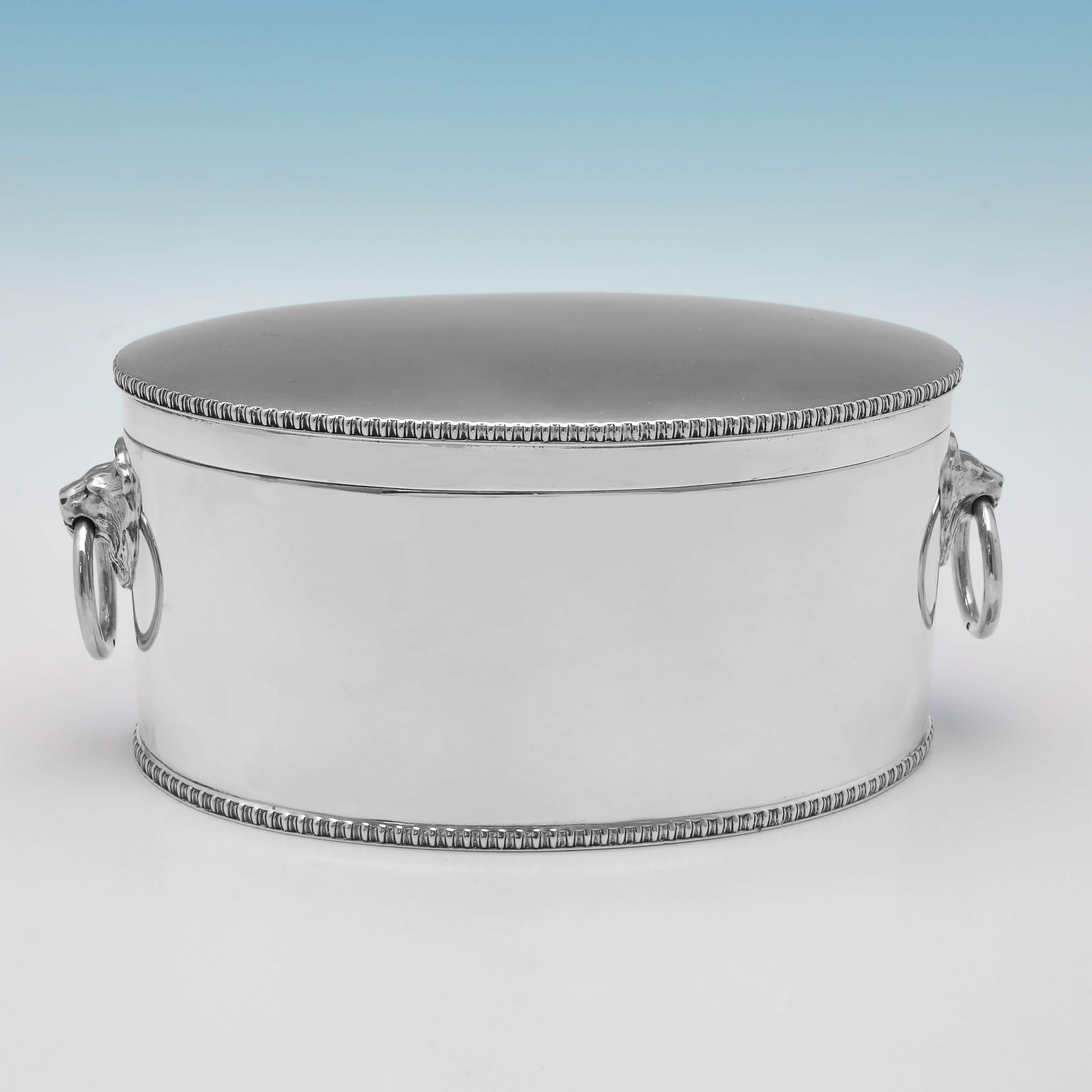 Hallmarked in Sheffield in 1930 by Atkin Brothers, this handsome, Sterling Silver Biscuit Box, is oval in shape, and features gadroon borders, and drop ring lion mask handles. The biscuit box measures 3.75