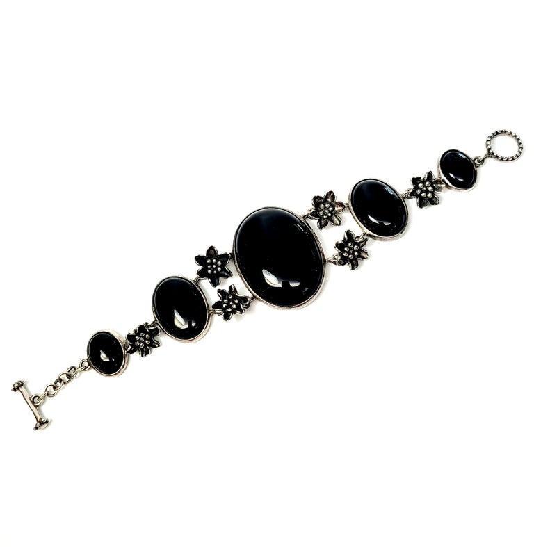 Sterling silver, onyx and flower link toggle bracelet.

Beautiful piece featuring large oval bezel set onyx stones alternating with small detailed flower links with a toggle closure that has silver beaded accents on each end of the toggle bar, as