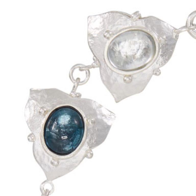 Sterling silver bracelet in a hammered finish featuring double-sided petals with gorgeous blue topaz stones in a variety of shades.  Please note this item is made to order and a similar but not identical piece can be made. Allow four weeks to