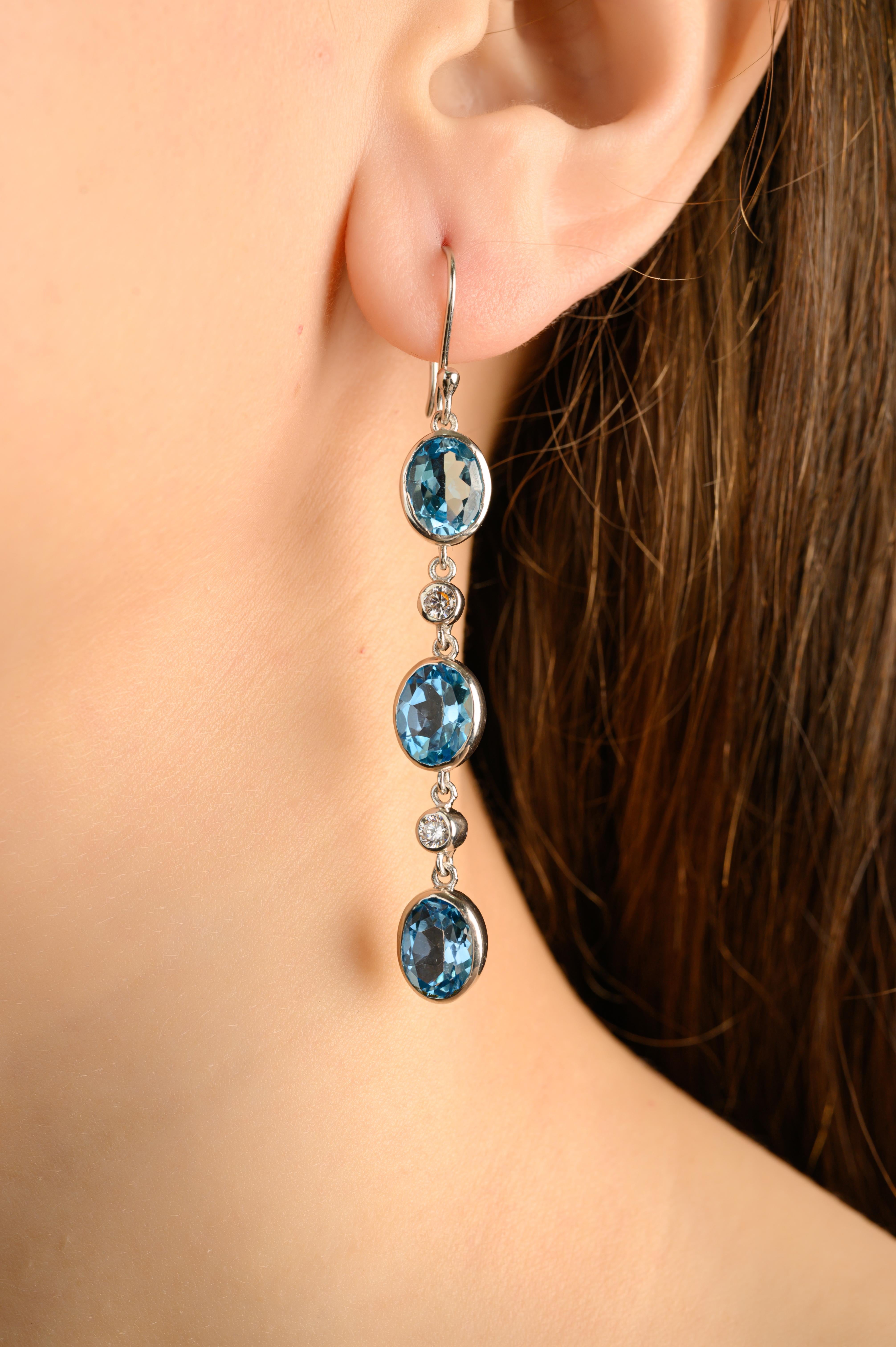 Questi orecchini a goccia lineari con topazio blu e zircone sono realizzati in luminoso argento 925 e presentano un affascinante trio di gemme di topazio blu dal taglio ovale, ciascuna incastonata per una silhouette pulita e moderna. Le scintillanti