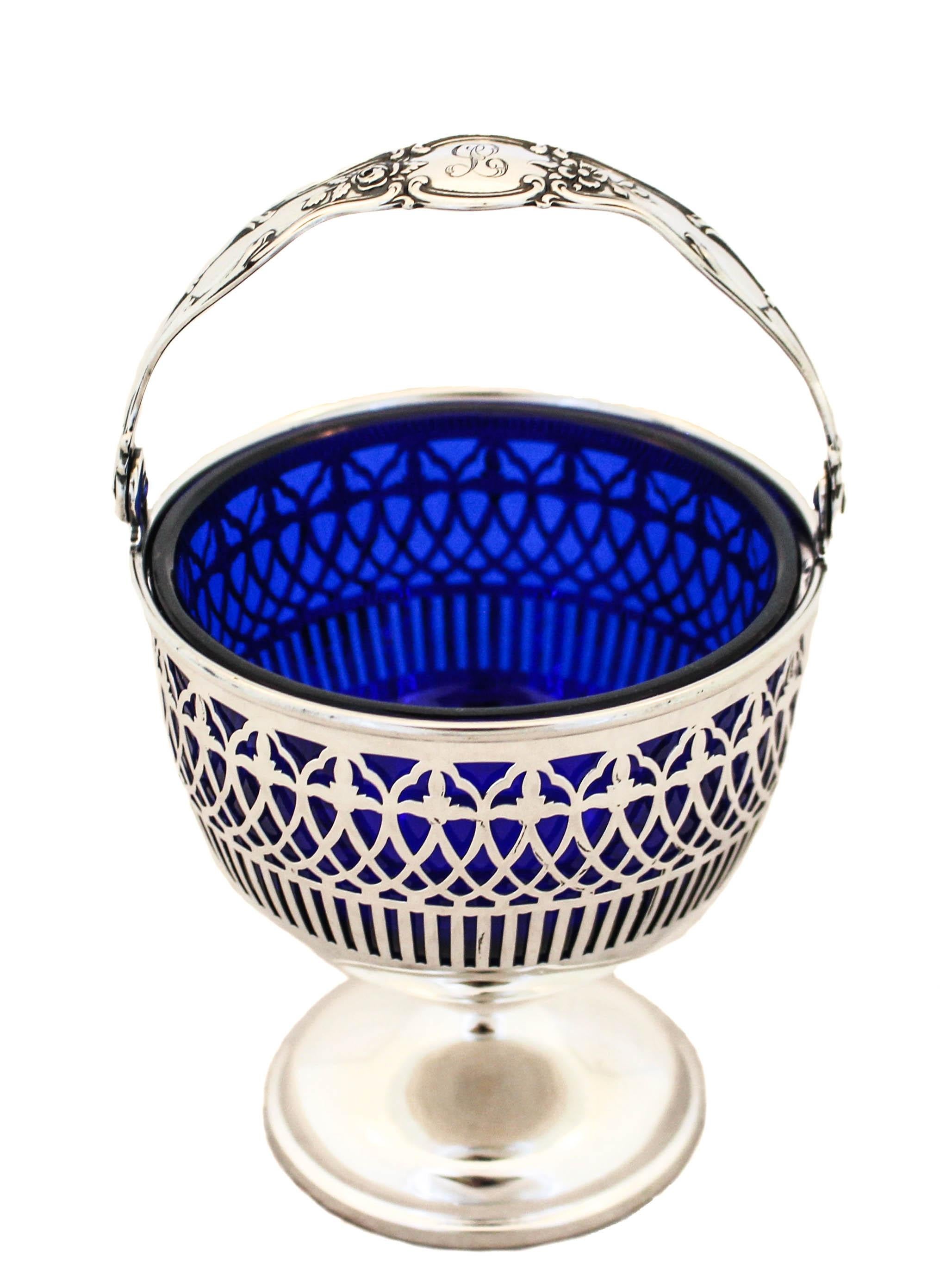 A beautiful sterling silver basket with a cobalt blue liner by Graff, Washbourne & Dunn. Standing proudly on a pedestal — not weighted, this basket has a reticulated pattern that allows the deep blue glass to shine through the sterling silver work.