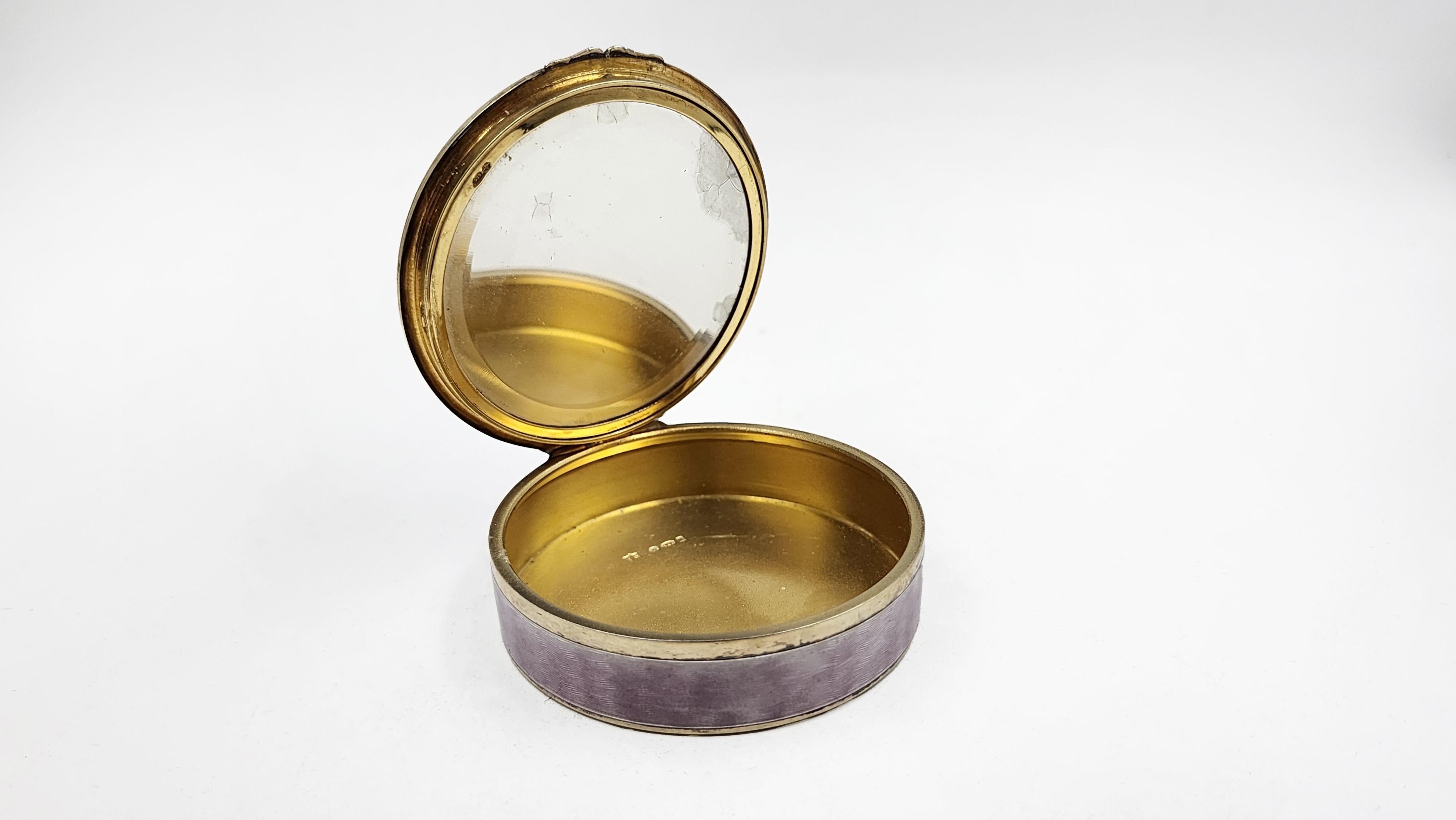 Sterling Silver Box with Enamel-Painted Scene
This round sterling silver box features a lid with a hand-painted enamel scene depicting a couple in a garden in a period style. The rim of the lid has an iridescent finish. The sides of the box are