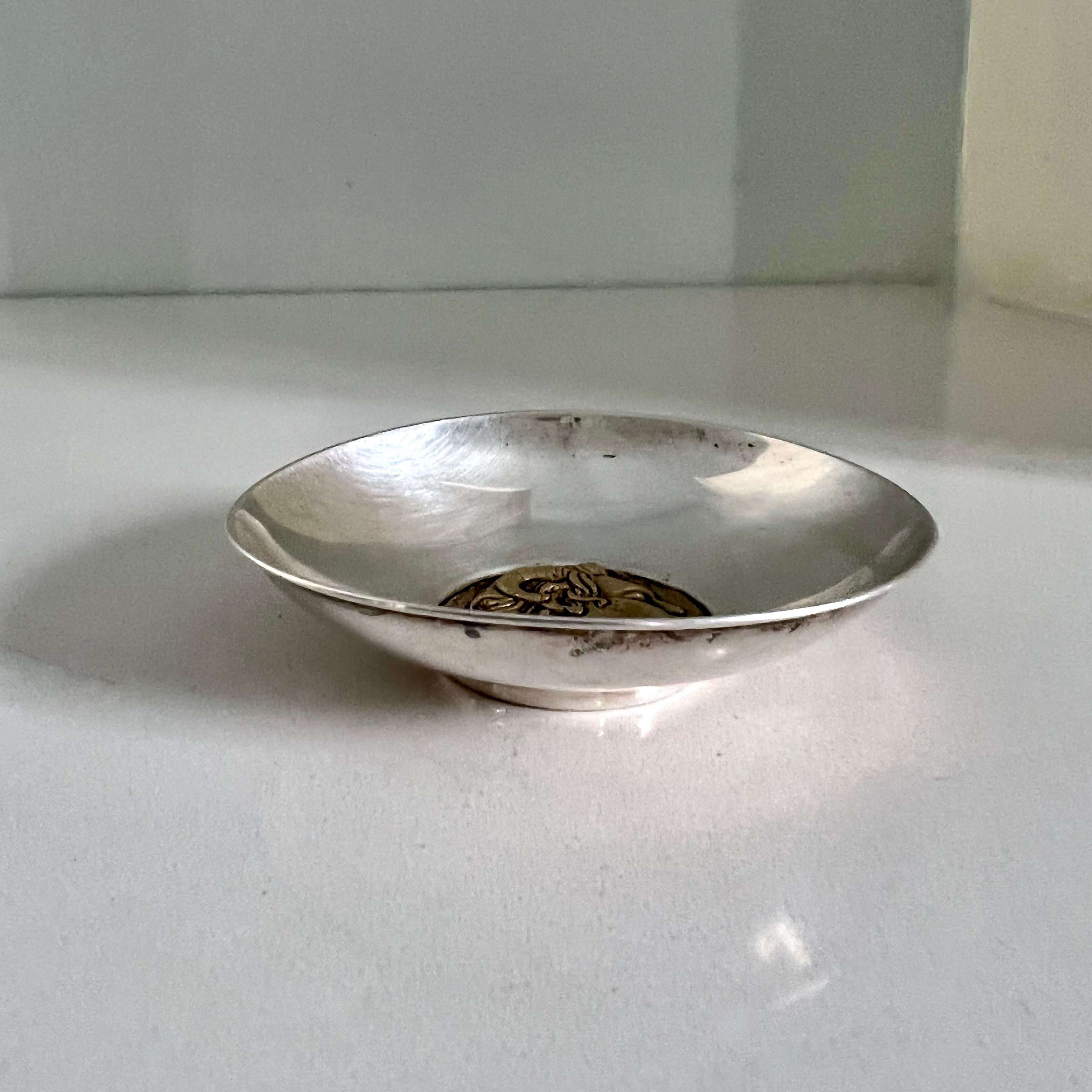 Polished sterling silver and brass trinket, coin or ring dish. Brass Satyr profile in brass at the base of the bowl is very detailed and impressive

Satyrs are woodland gods seen as symbols of fertility.