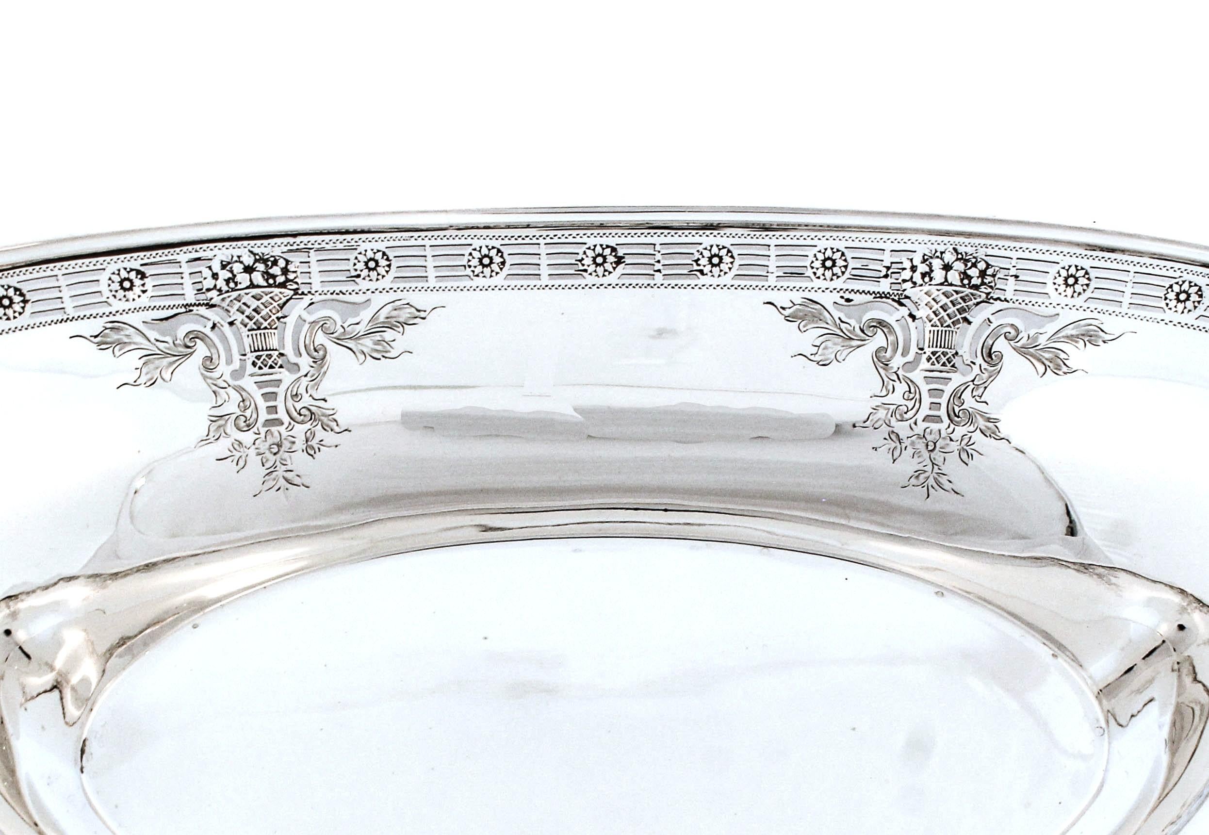 Se ofrece una panera de plata de ley de Dominick & Haff.  Tiene la elegancia del viejo mundo con su cesta de flores alrededor del borde y un diseño reticulado a lo largo del borde.  Seis cestas de flores están rodeadas de hojas grabadas y guirnaldas