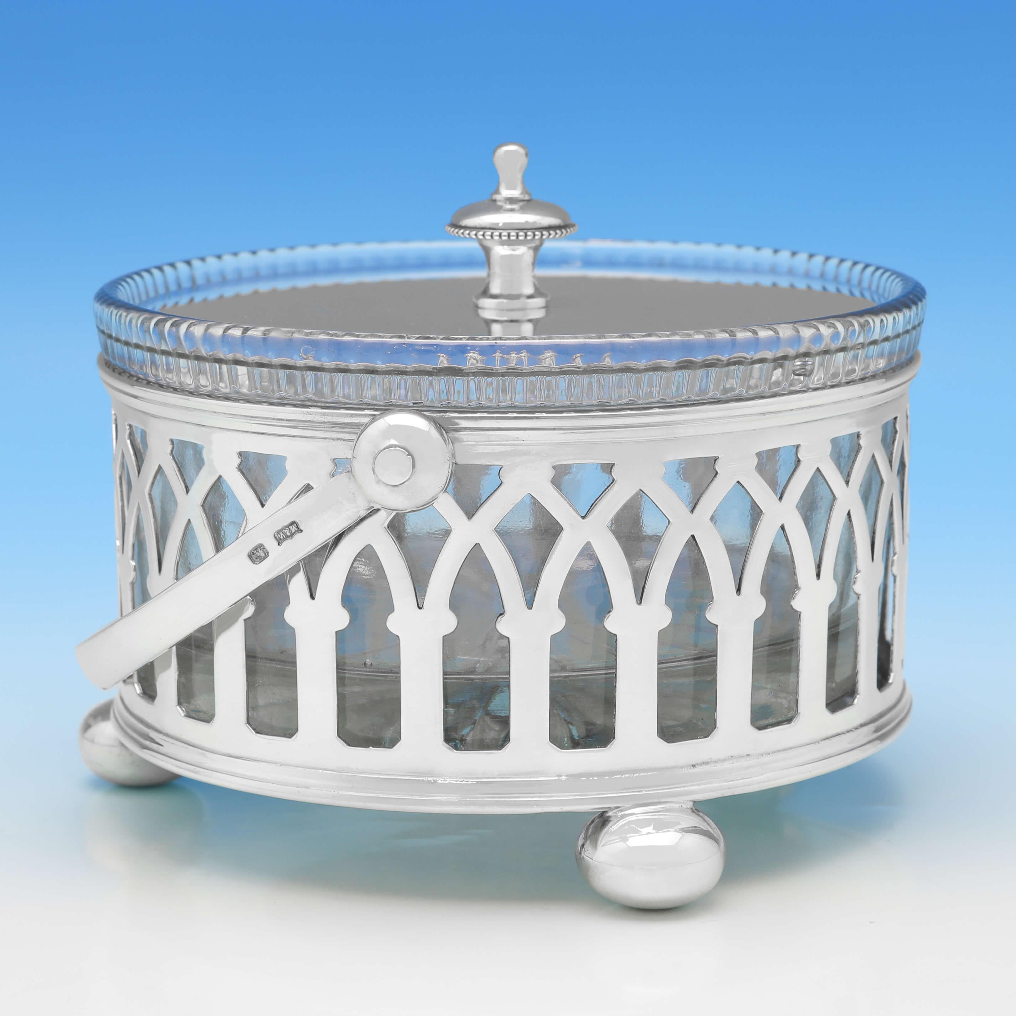 Hallmarked in Sheffield in 1915 by Mappin & Webb, this handsome, antique sterling silver butter dish, stands on ball feet, and features Gothic revival pierce work to the sides, a swing handle, and a glass liner. The butter dish measures 4
