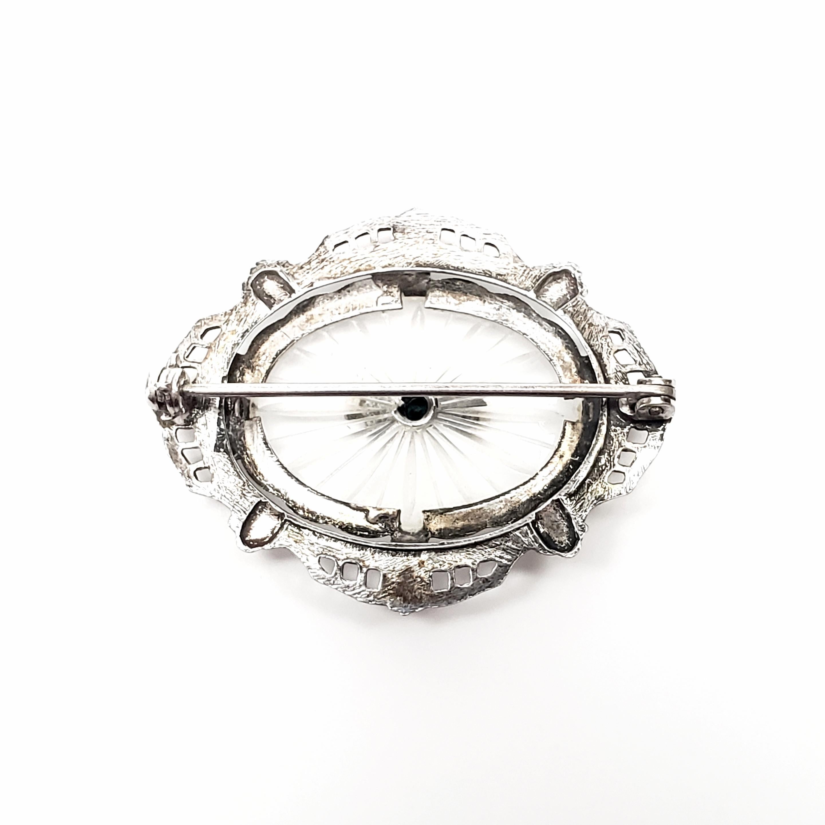 Vintage sterling silver diamond and camphor glass pin.

Beautiful art deco design features oval camphor glass with a starburst design and a small round diamond, bezel set in an ornate sterling silver frame.

Measures 1 1/4