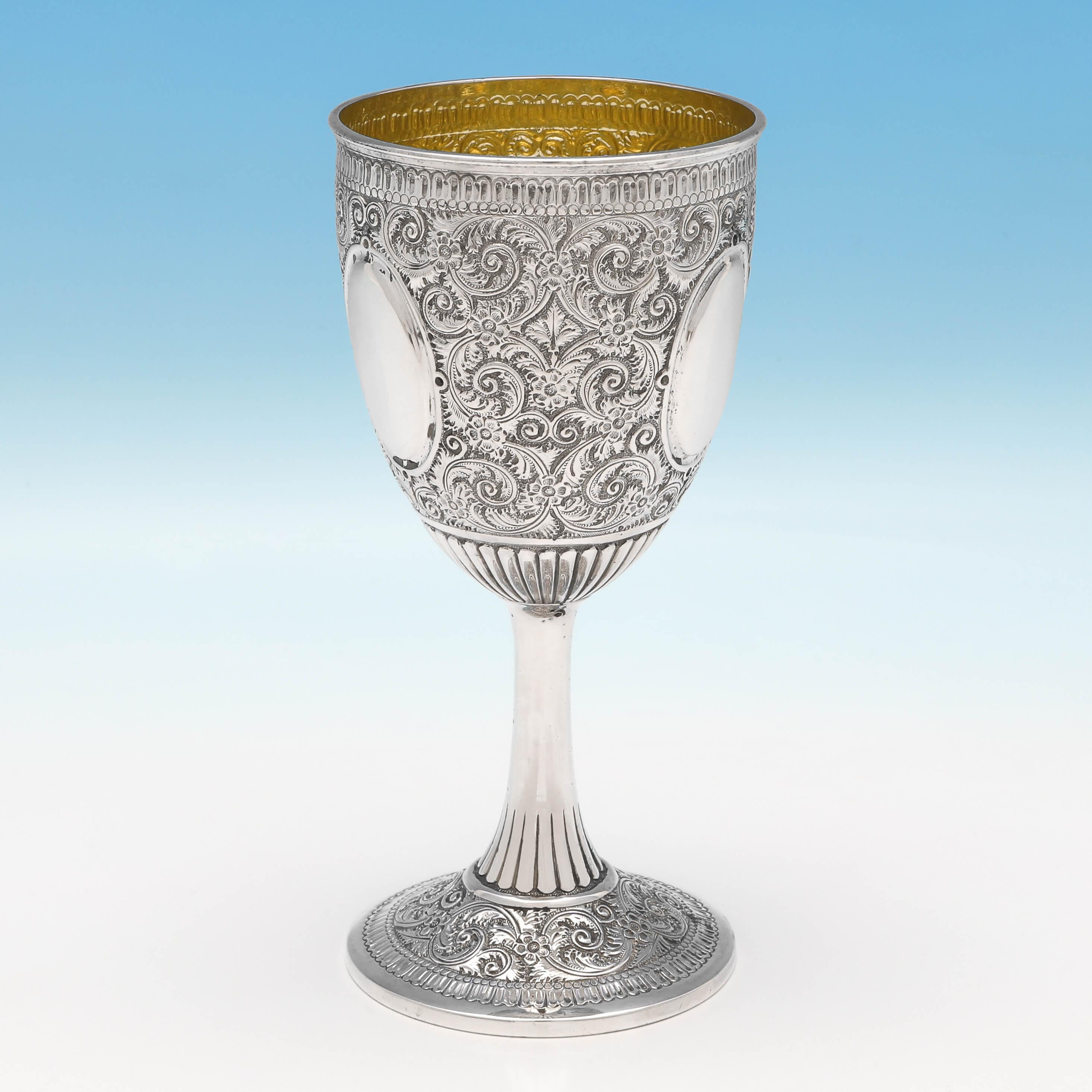 Hallmarked in Sheffield in 1881 by Sibray, Hall & Co., this striking, Victorian, antique sterling silver goblet, features intricate chased decoration throughout, fluted detailing, and a gilt interior. The goblet measures 6.5