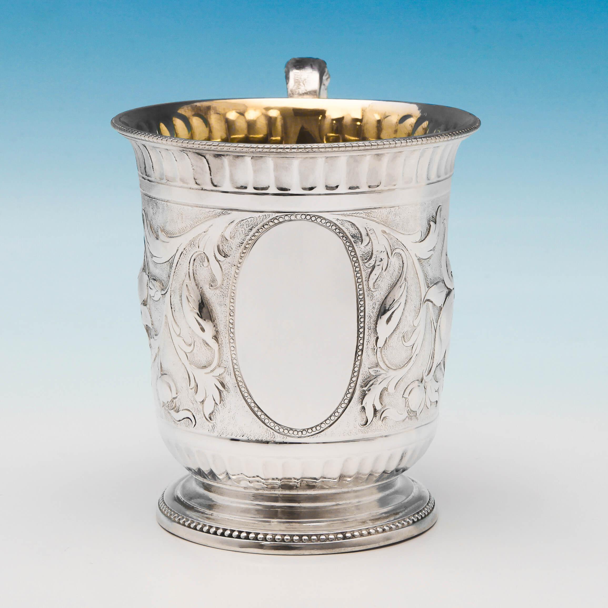 Hallmarked in London in 1867 by Samuel Smily, this striking, Victorian, antique, sterling silver Christening mug, features chased naturalistic decoration, an acanthus detailed scroll handle, and a gilt interior. The christening mug measures: 3.75