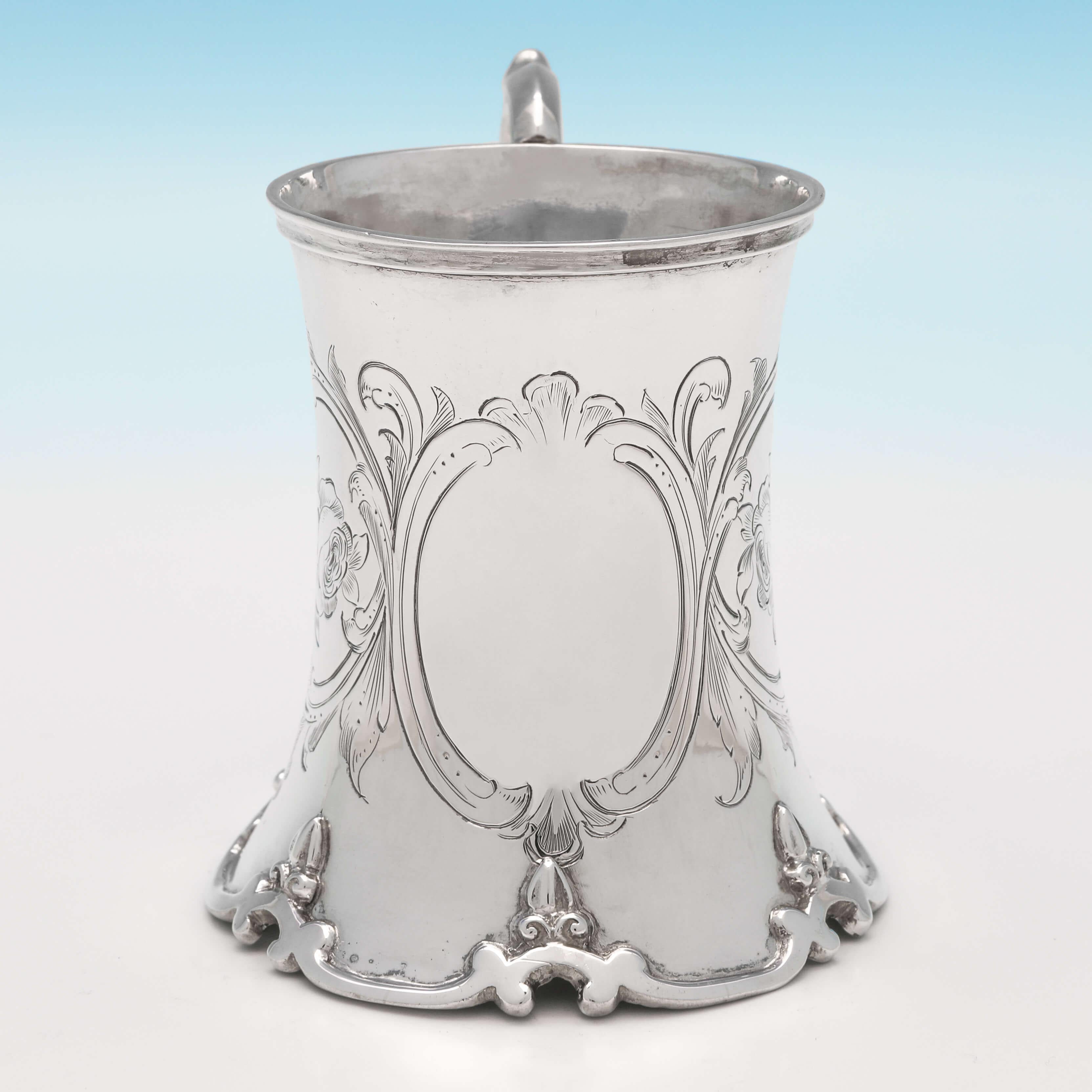 Hallmarked in London in 1852 by Robert Hennell IV, this elegant, Victorian, antique sterling silver Christening mug, has concave shaping with a scroll base, engraved decoration, a scroll handle and a gilt interior. The christening mug measures