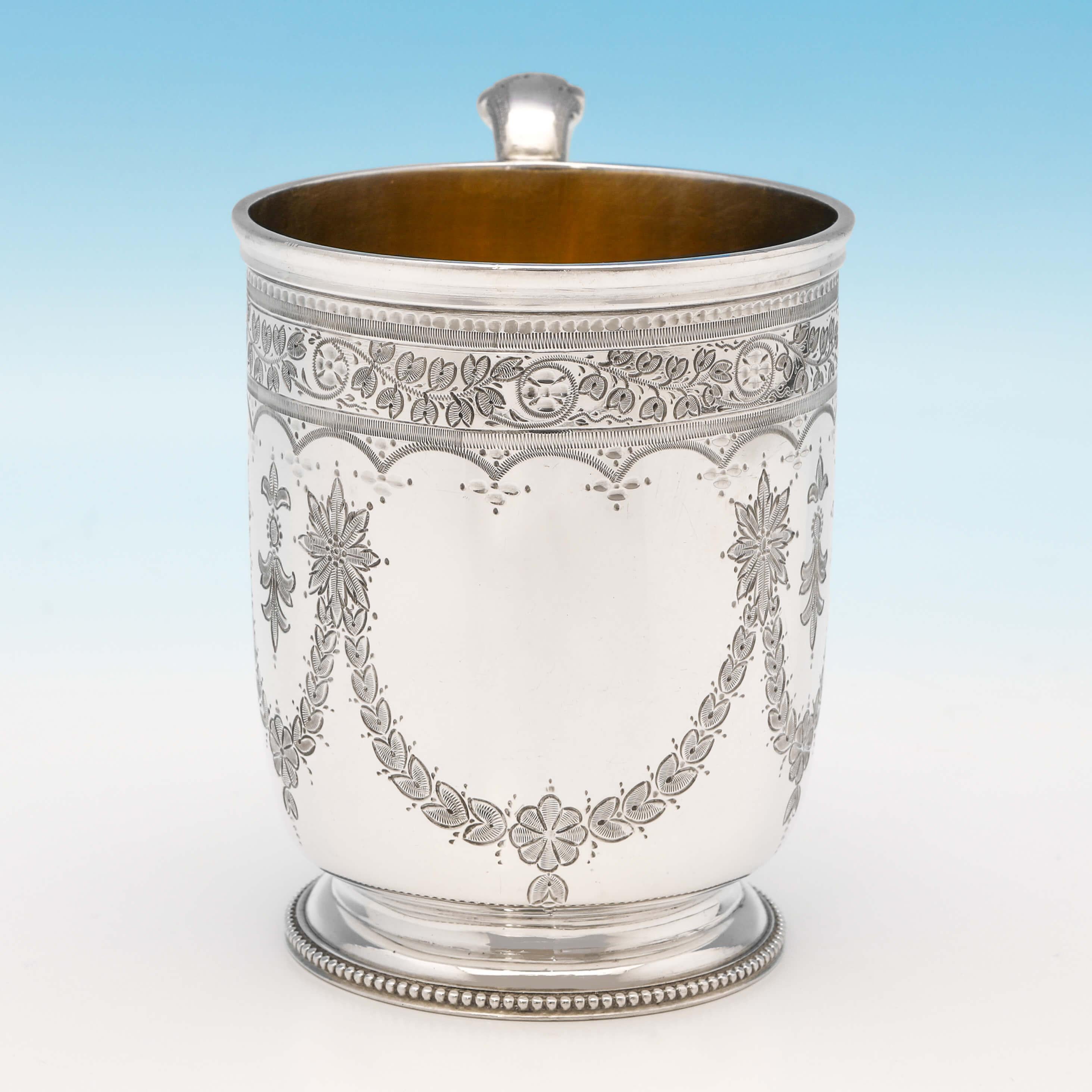 Hallmarked in London in 1872 by Henry Wilkinson & Co., this attractive, Victorian, antique sterling silver christening mug, features striking engraved decoration, a bead bordered base, an acanthus handle and a gilt interior. The christening mug