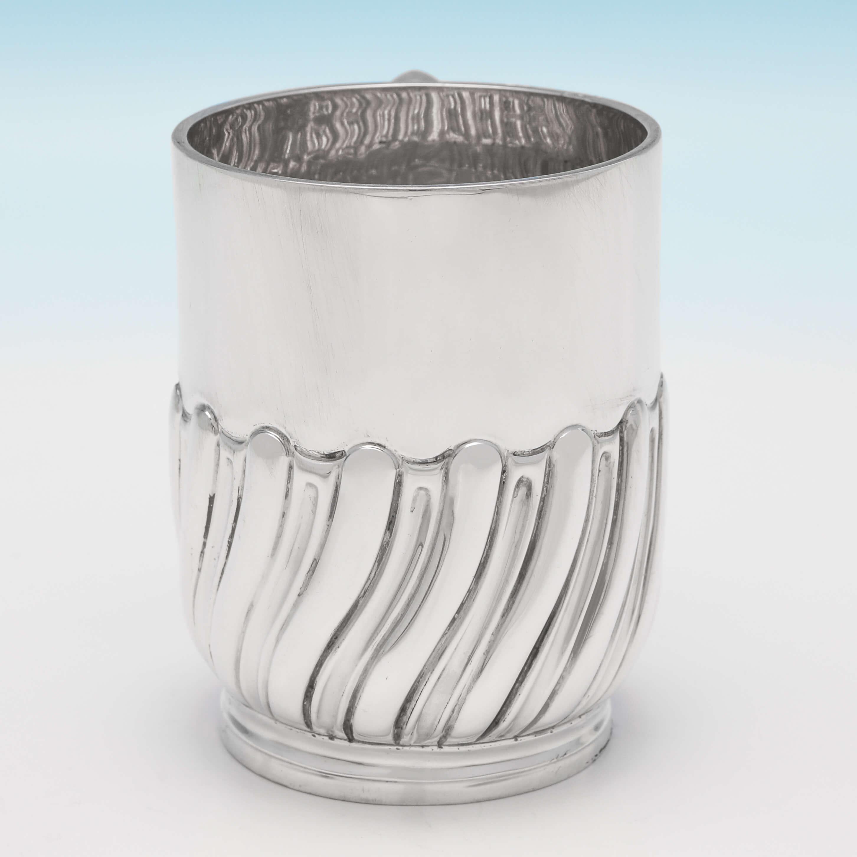 Hallmarked in London in 1898 by Jackson & Fullerton, this handsome, Victorian, antique sterling silver Christening mug, features swirled half fluted decoration and a plain loop handle. The christening mug measures 3.25