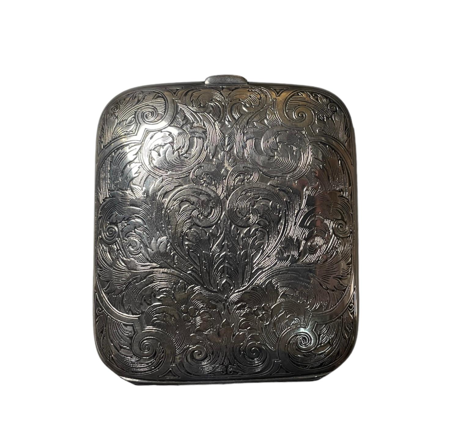 This is a Sterling Silver Case Travel Eight Days Clock. It depicts a sterling silver clamshell case engraved with multiple scrolls of acanthus leaves that in the front center they form a heart and in the back, a shield. The inside of the case