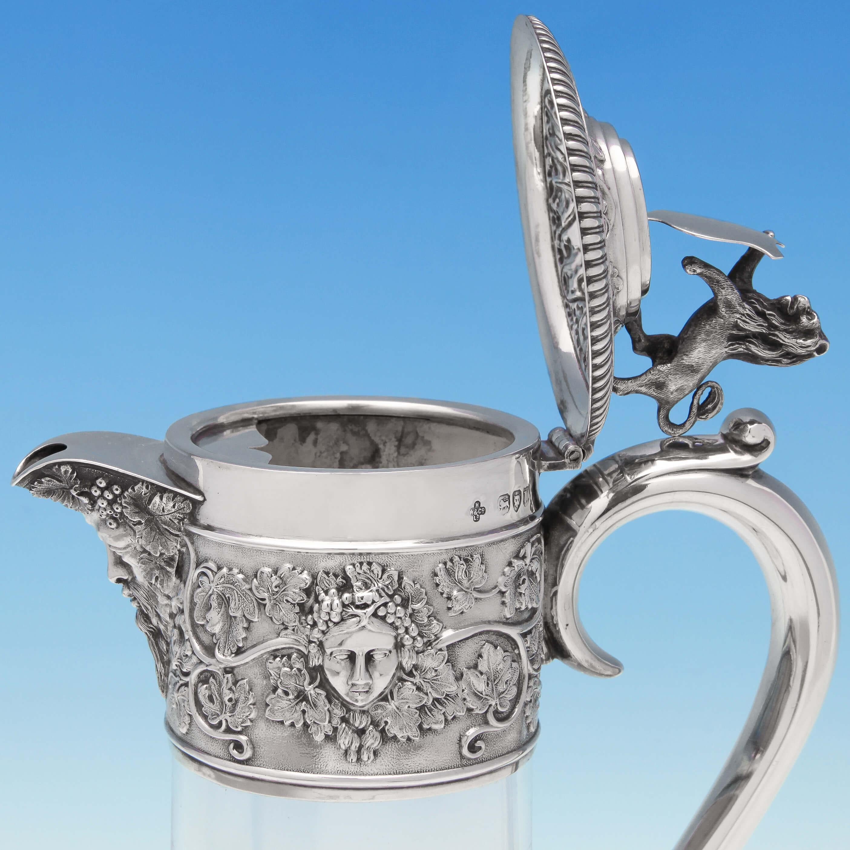Hallmarked in London in 1895 by Horace Woodward & Co., this fine Antique, Victorian, Sterling Silver Claret Jug comprises of a plain glass body with an elaborately chased silver mount featuring grape and vine decoration, Bacchus masks and a finial