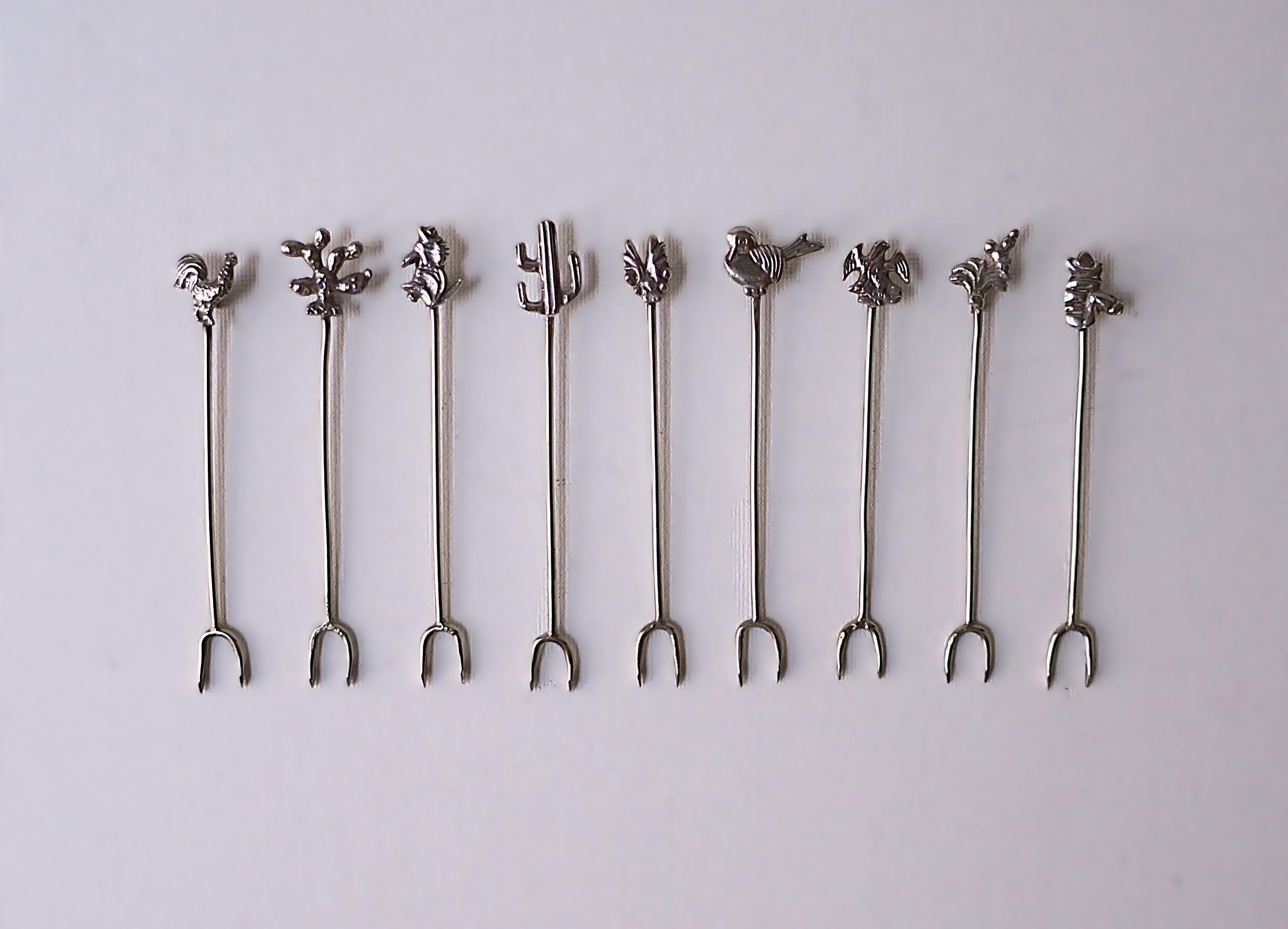 Un magnifique ensemble de neuf (9) fourchettes/pics à cocktail ou à apéritif en argent sterling mexicain avec des dessus charmants, vers le milieu du 20e siècle, Mexique. Les charmes comprennent un coq, un cactus x2, un amigo avec sombrero, un