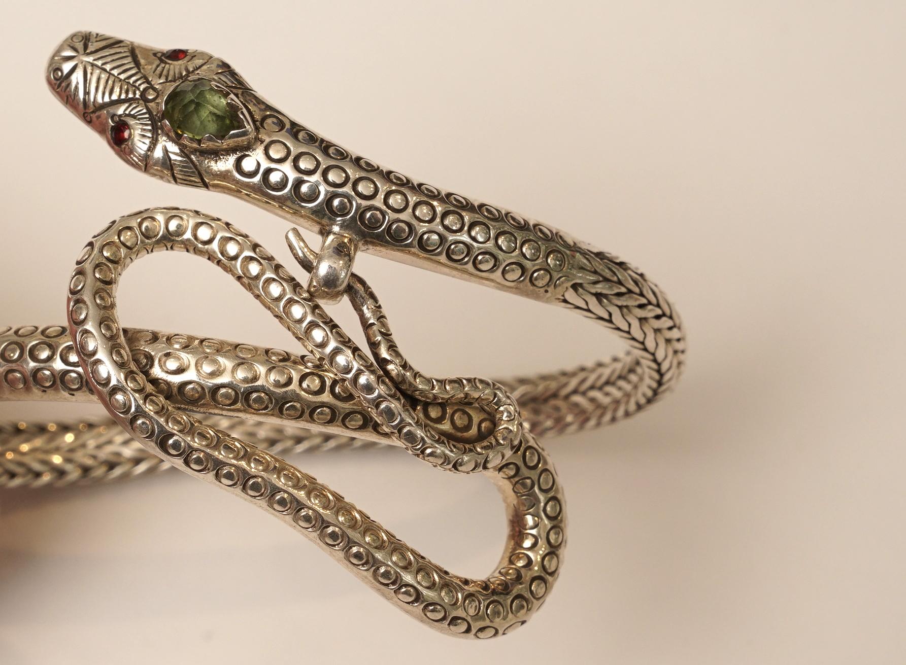 Finely tooled sterling silver coiled snake bracelet with garnet eyes and peridot third eye. The tail of the snake pushes through the ring just below the head of the snake.  Unusual.  The inside circumference is 6 inches.
The height is 1.5 inches.
