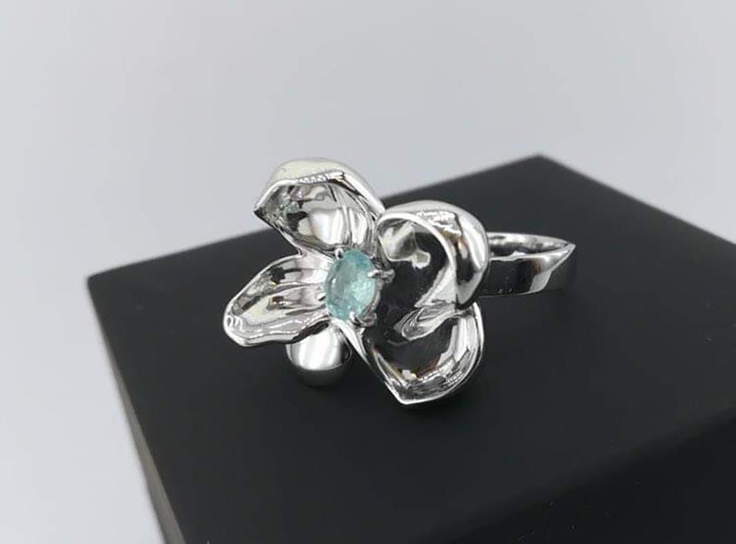 This Magnolia Flower contemporary cocktail ring is in sterling silver with an oval copper-bearing Paraiba tourmaline weighing 0.28 carats. The water surface of the gem multiplies the light, mirroring on the golden petals. The weight of the ring is