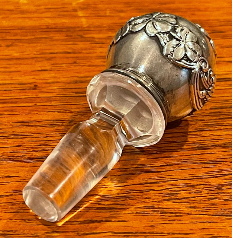 A very rare and hard to find sterling silver and crystal bottle stopper by Tiffany & Co., circa 1940s. The piece has a floral sterling silver overlay on a crystal bottle stopper and is stamped on the side “Tiffany & Co. Makers Sterling”. The piece