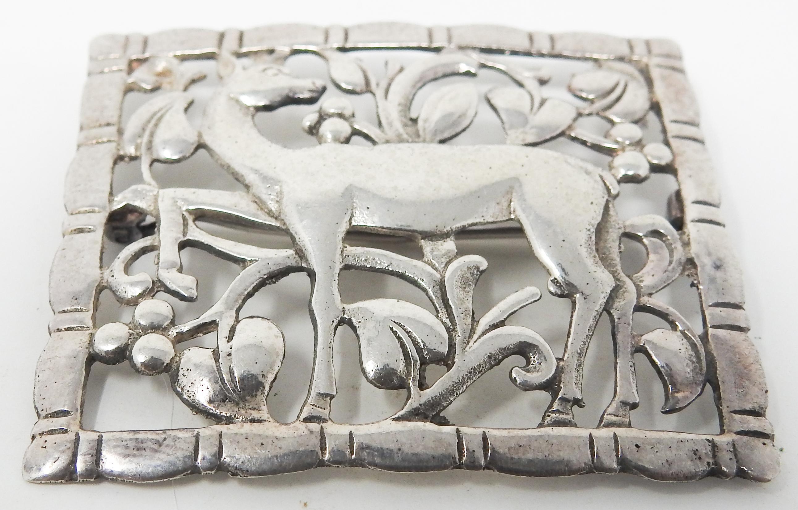 Offering this elegant sterling silver brooch with deer. The deer is depicted standing looking over its back. The background is openwork that is foliate detail. The edge is a simple scalloped edge. The back of the brooch is marked Sterling.