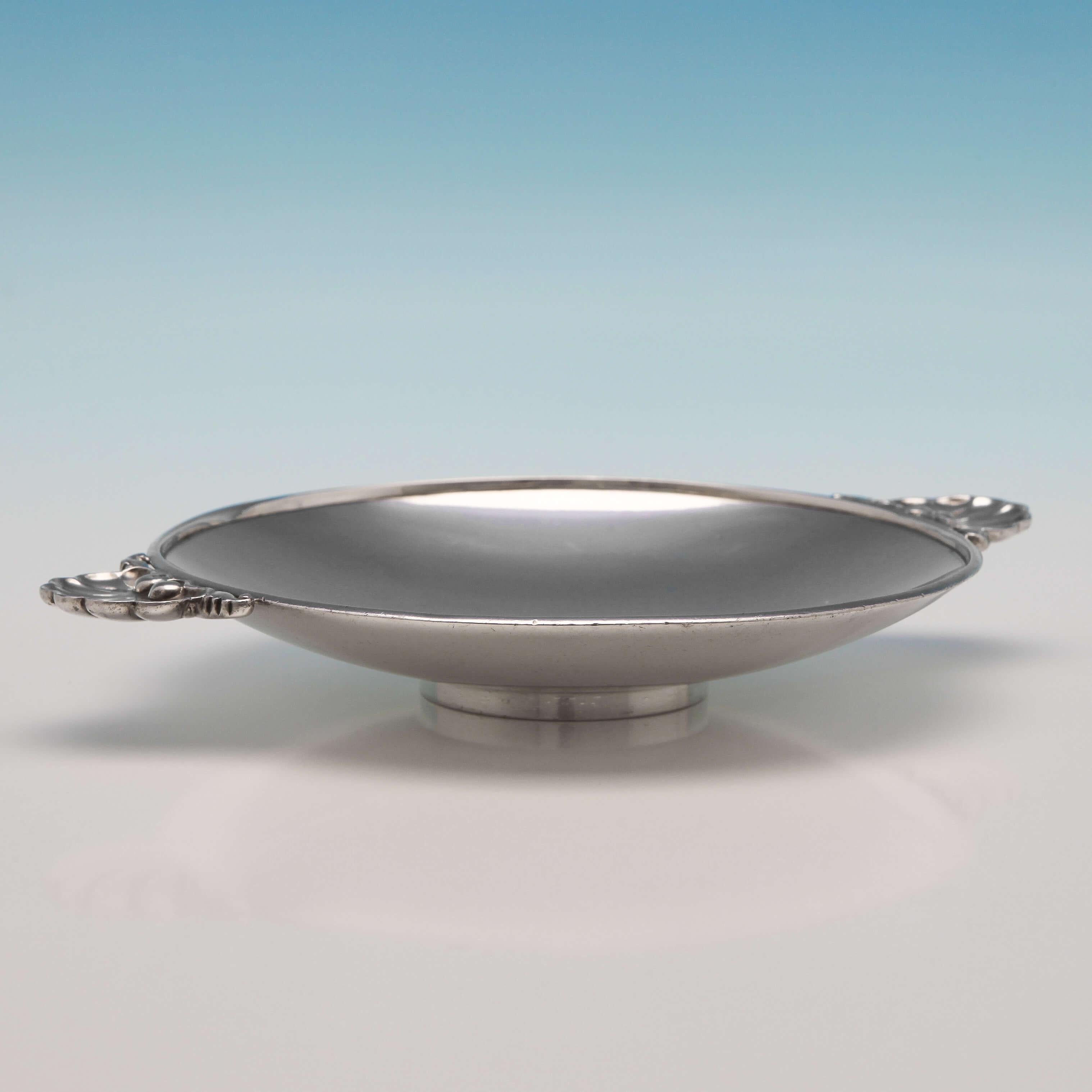 Made circa 1950 in Denmark by Georg Jensen, this lovely sterling silver dish has a plain, shallow bowl with two applied shell and scroll handles, and stands on a pedestal base. The dish measures 6.25