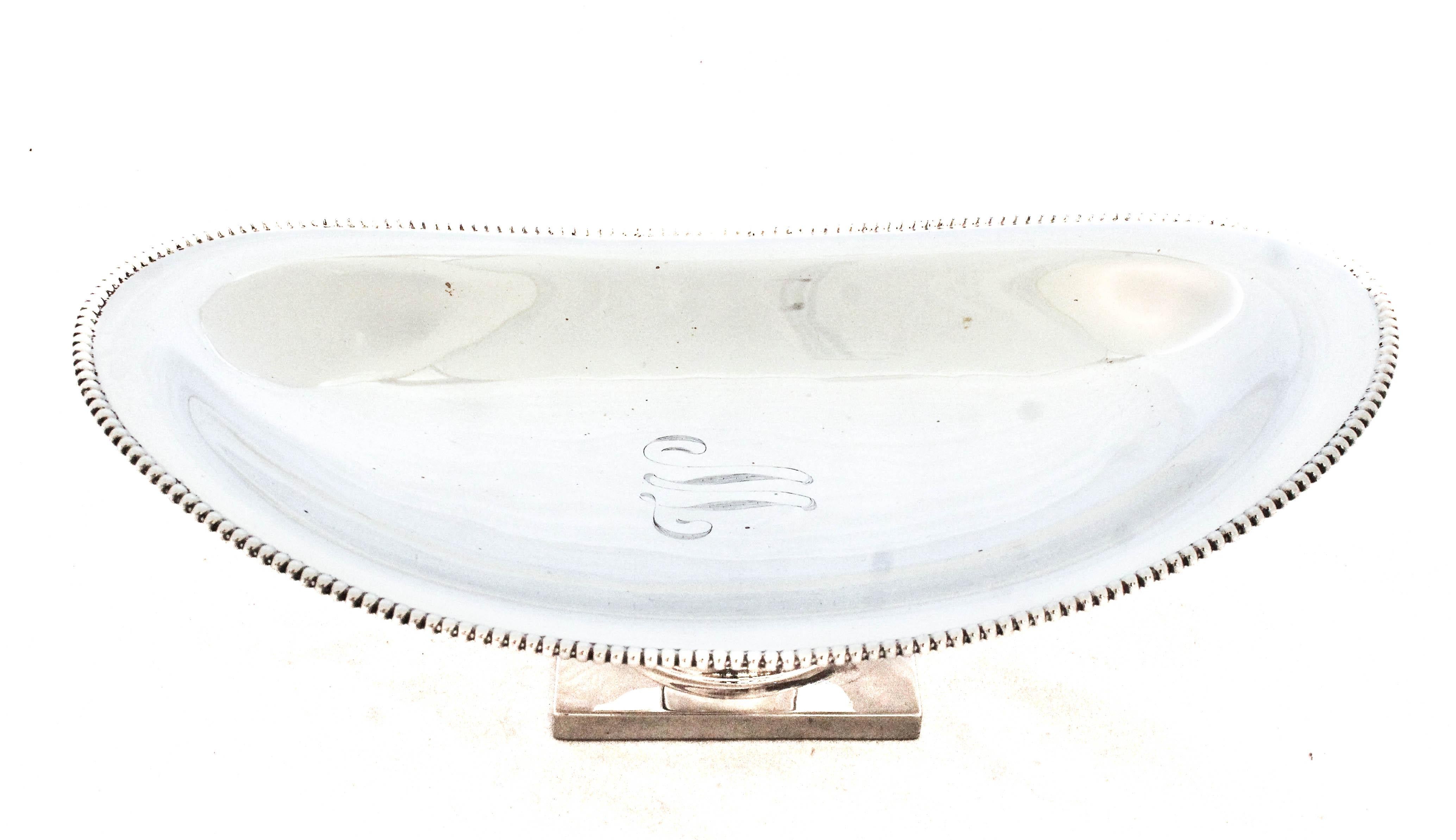 Se ofrece un plato de plata de ley de Wallace Silversmiths.  Sobre un pedestal cuadrado de estilo neoclásico, el plato es ovalado y tiene el borde rebordeado. Sencillez y sofisticación en esta discreta pieza de plata. 