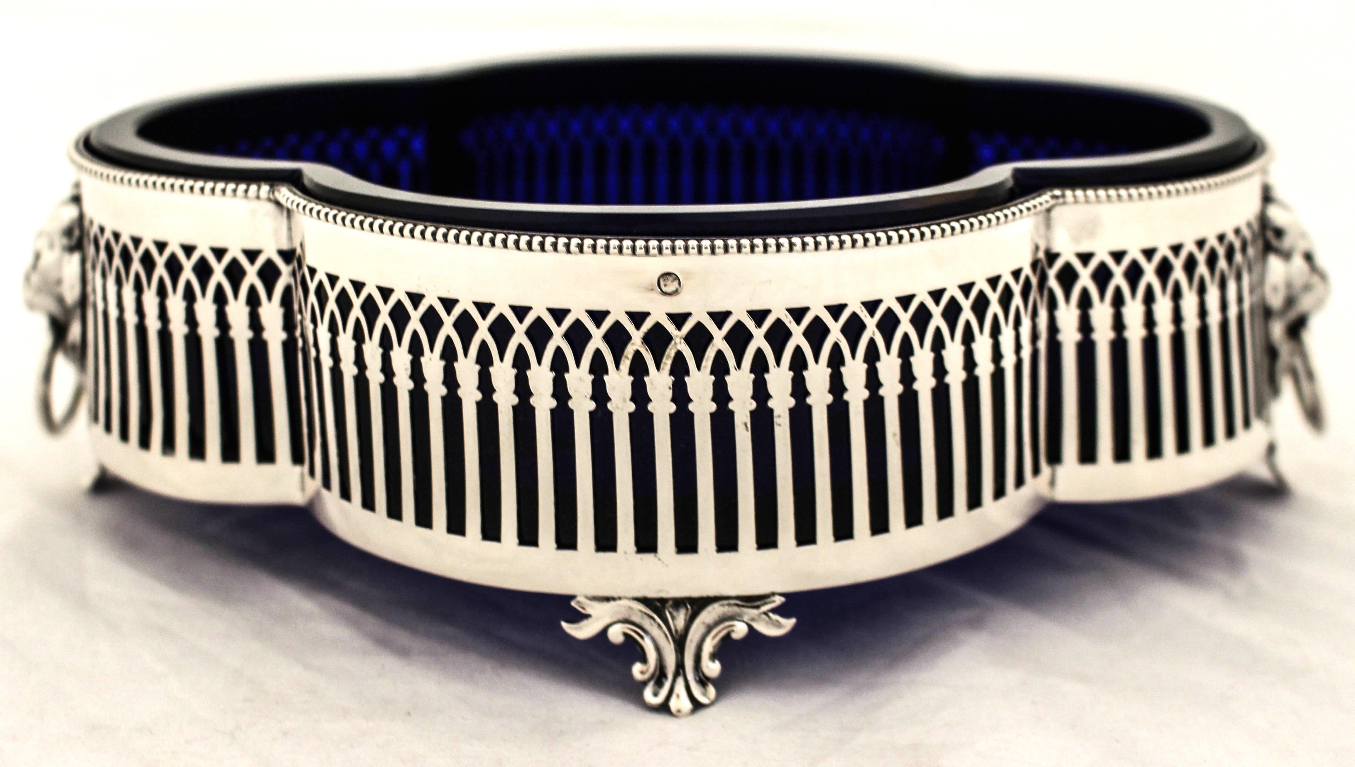 Being offered is a sterling silver bowl with a cobalt glass liner made in Holland.  The shape is scalloped and the silver is reticulated with a lions head on each end with a ring in its mouth.  It stands on four feet thereby propped off the surface.