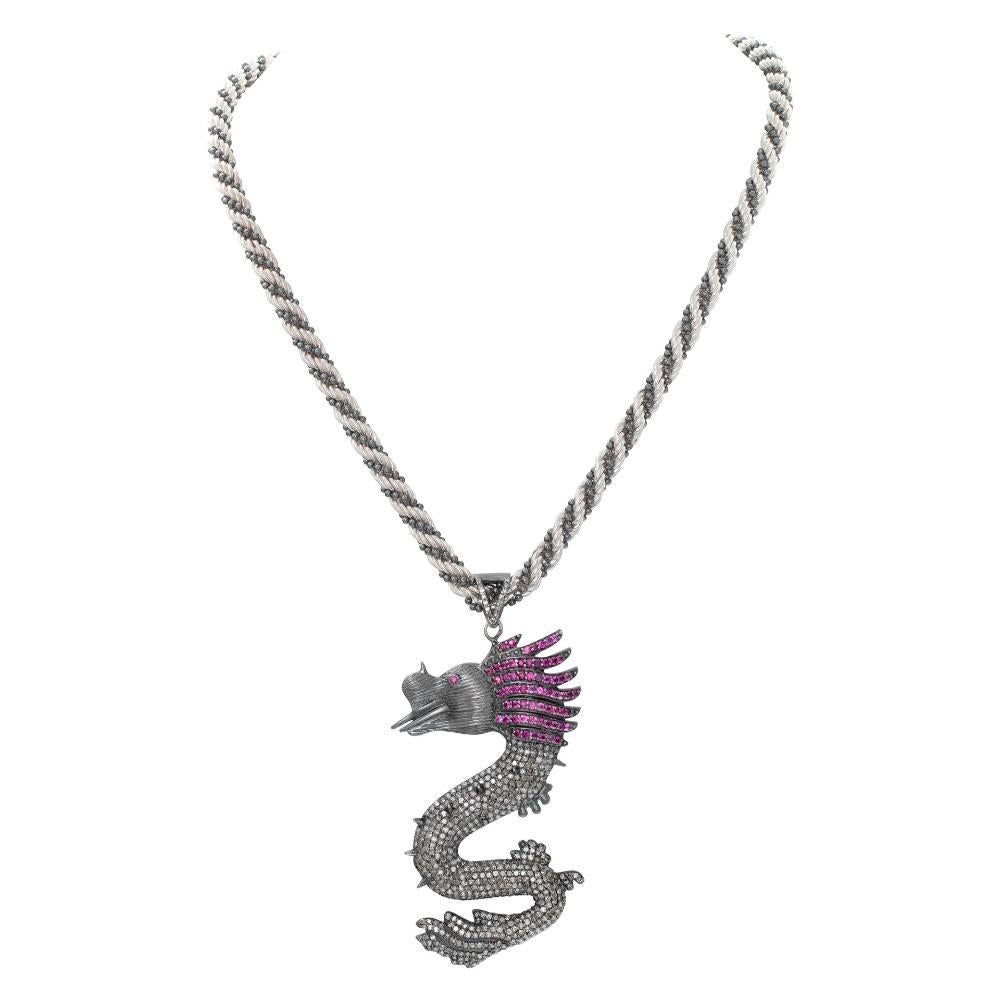 Dragon Pendant in sterling silver with approx 1 ct of rubies and 2.5 cts of diamonds on a sterling silver rope chain. Blackened to highlight red and white precious stones. Rope chain has highlights with black accented beads. Total length including