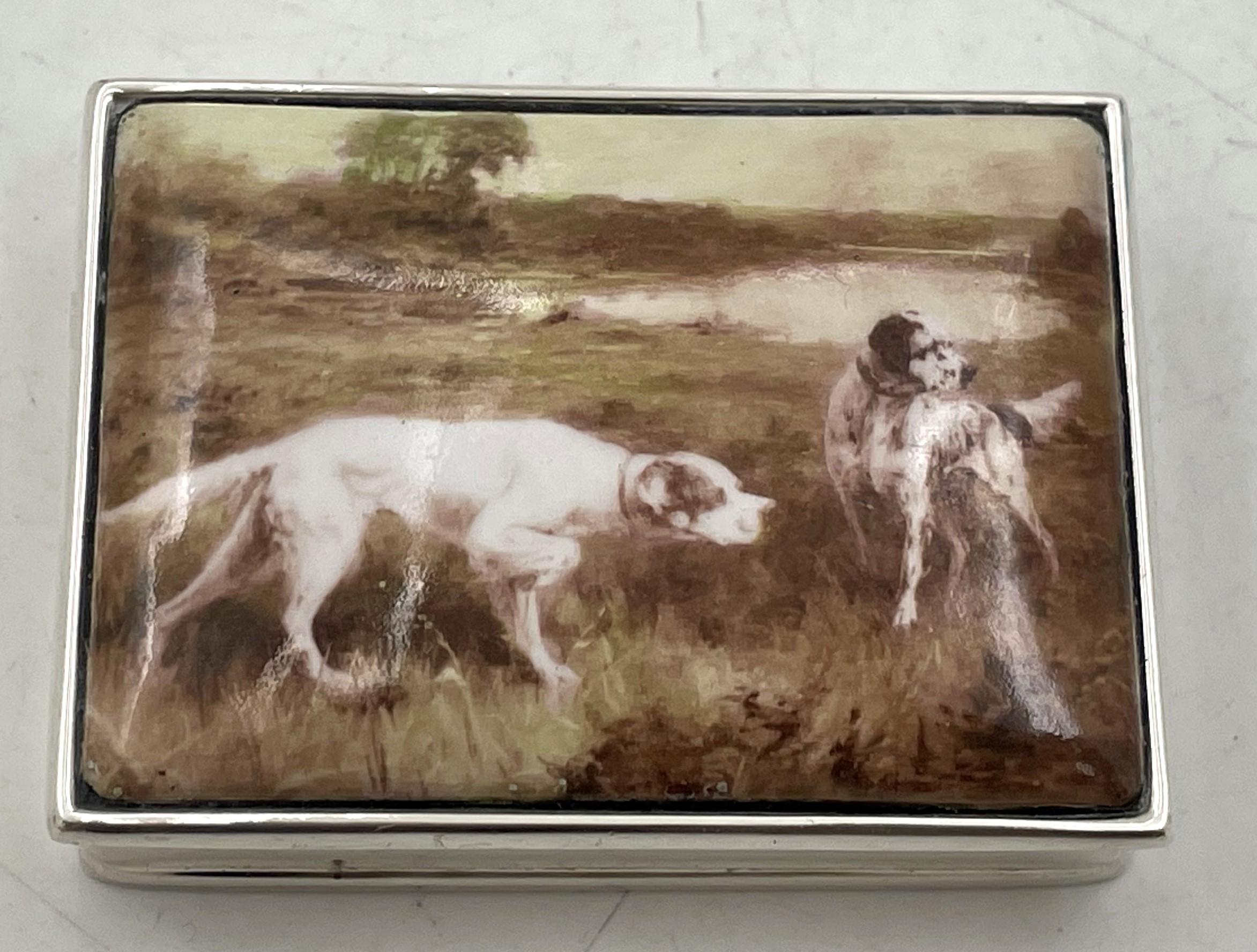 Pastillero de plata de ley con una placa de esmalte aplicado en la parte superior que representa perros en un paisaje. Mide 2 1/4'' por 1 2/3'' por 3/4'', pesa 2 onzas troy y lleva los sellos que se muestran. 

No dude en hacernos cualquier pregunta