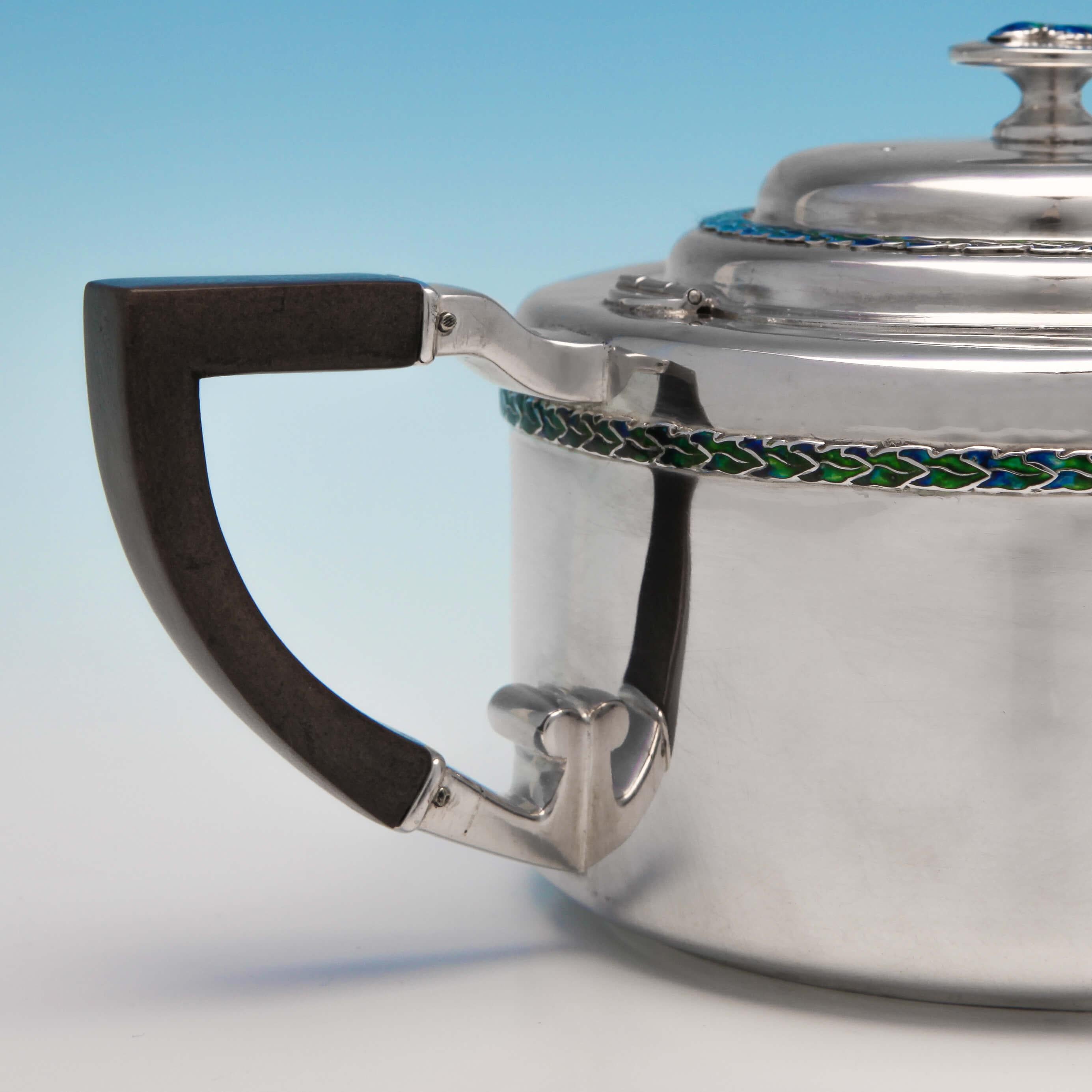 Hallmarked in Birmingham in 1909 by Liberty & Co. This exquisite Edwardian, antique, sterling silver teapot is in the Arts & Crafts style. It has been embellished with two bands of enamel and an enameled finial in the Classic liberty blue and green