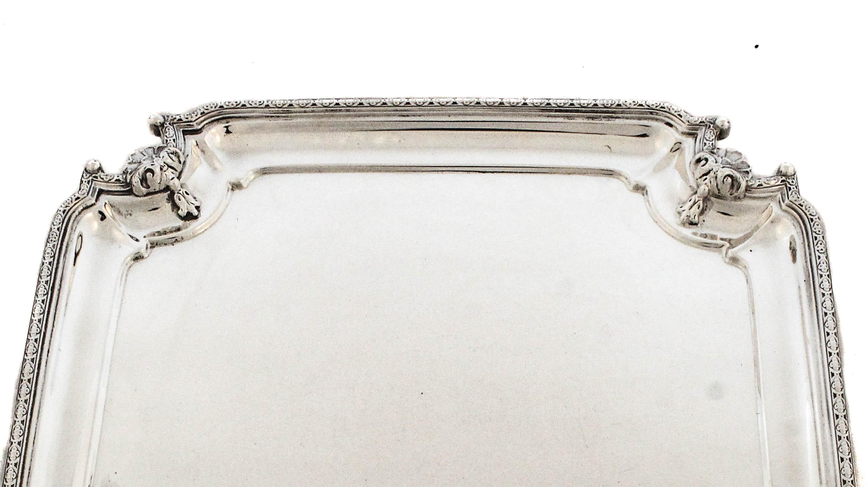 Questo straordinario salver inglese in argento sterling ha una forma quadrata con angoli elegantemente inclinati, che gli conferiscono una presenza raffinata e maestosa. Ogni angolo è ornato da intricate decorazioni applicate, con maschere classiche