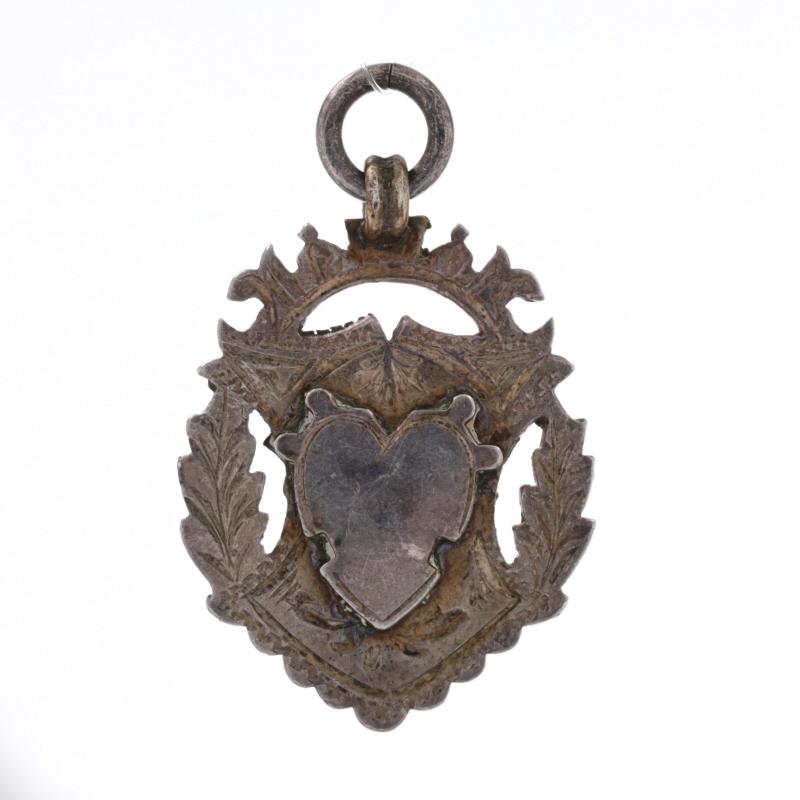 Brand: Herbert Bushell & Son Ltd
Date: 1912 - 1913

Metal Content: Sterling Silver

Style: Fob
Theme: Heart Shield Crest
Features: Engravable heart & shield centers with etched borders

Measurements
Tall (from stationary bail): 1 5/16