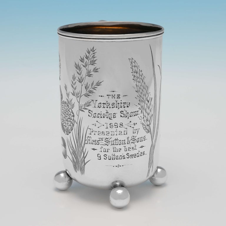 Hallmarked in Birmingham in 1895 by Barker Brothers Ltd., this very attractive, Victorian, antique sterling silver mug, stands on 3 ball feet, and features a loop handle, a gilt interior, and wonderful engraved decoration. The mug measures 5