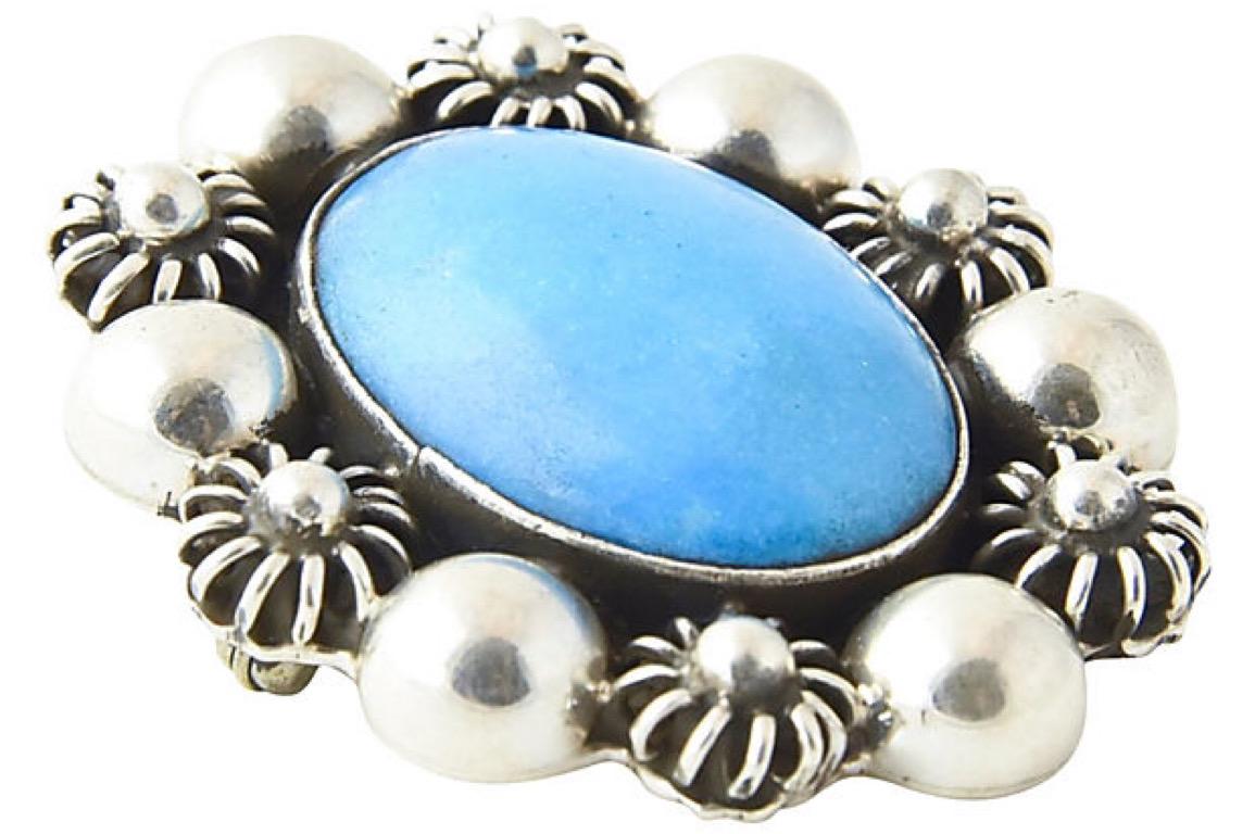 Lovely Mexican brooch featuring a cabochon man made turquoise oval piece in a sterling silver frame decorated with smooth balls and flowers. Stamped: TC 275 Mexico 925. 20th century style.