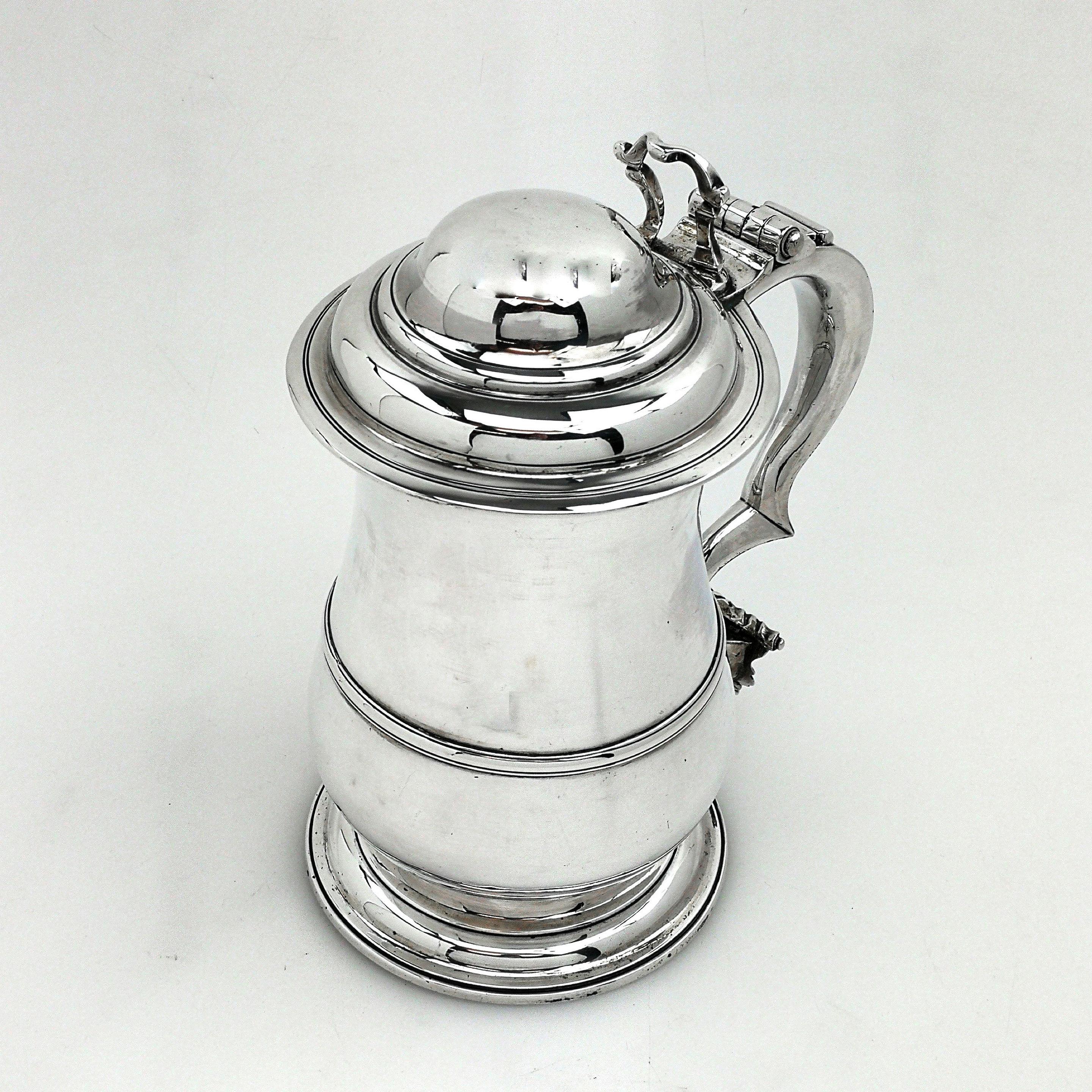 A classic antique George II solid silver lidded tankard. This silver Georgian Quart tankard has an impressive domed hinged lid with a shaped thumb piece and a substantial scroll handle. The Tankard has a traditional baluster shape with an applied