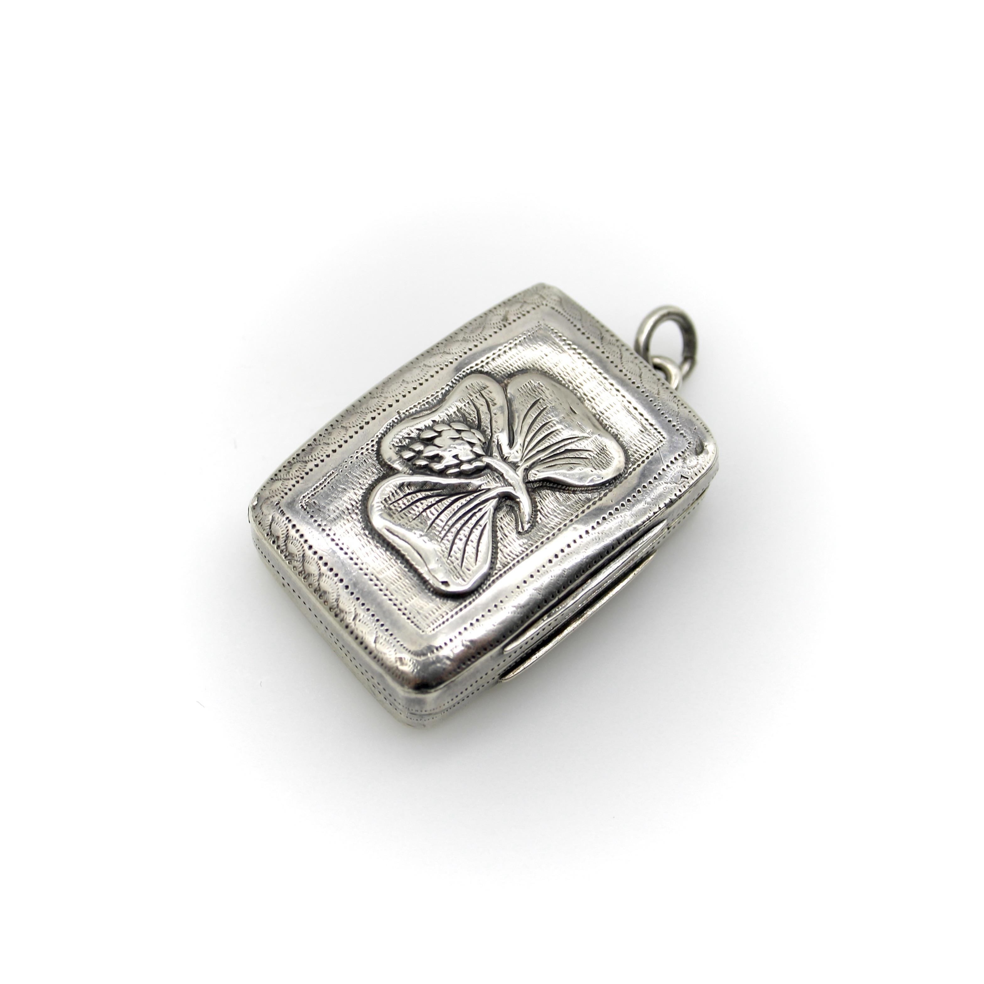 This sterling silver Georgian vinaigrette has a bas relief floral design on its lid of a three-leaf clover with a bloom in the center. Around the clover is delicate hand-engraved ticking that creates a rectangular border. The bottom of the box is