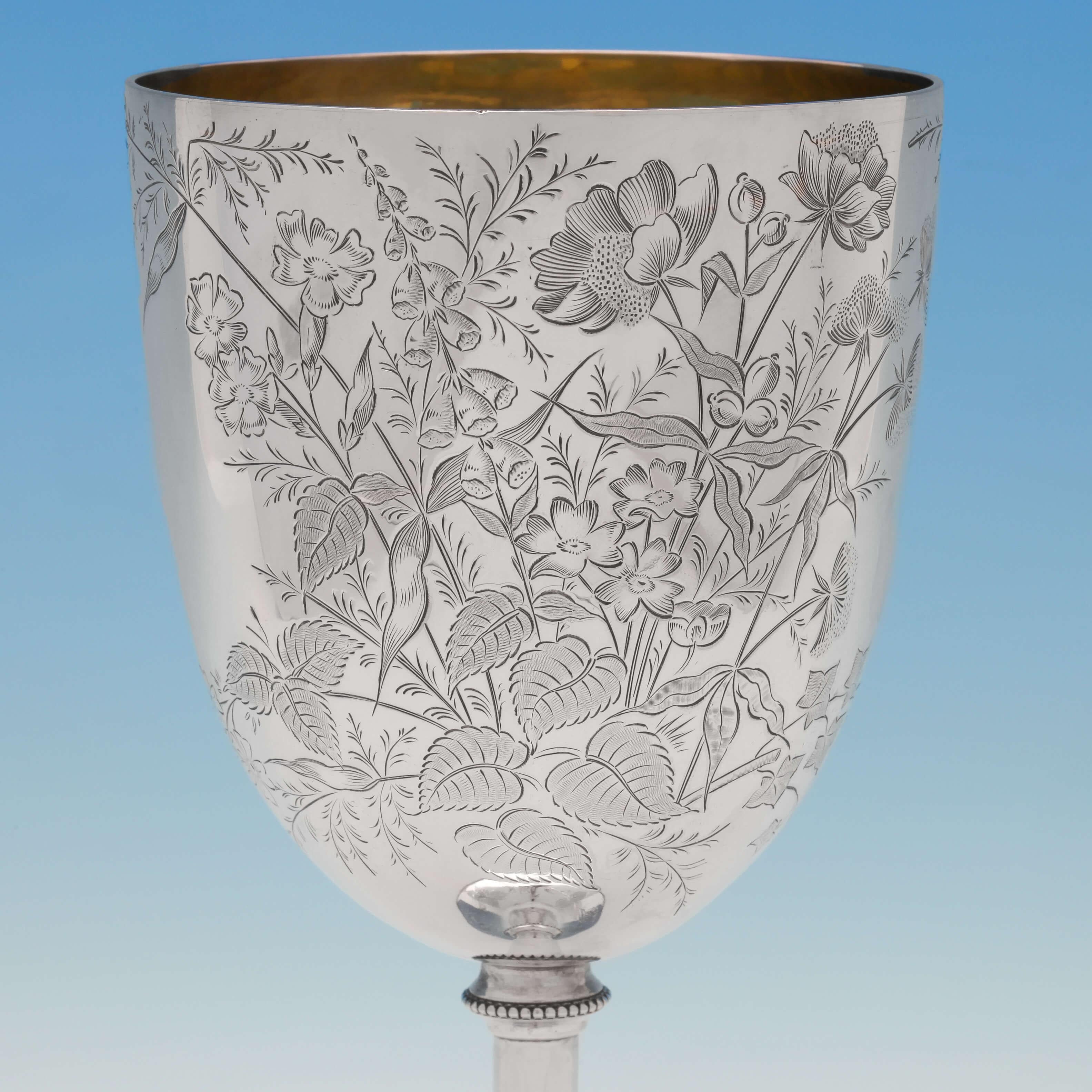 Hallmarked in Sheffield in 1887 by W. W. Harrison, this attractive, large, Victorian, antique, sterling silver goblet, features naturalistic engraving throughout, a bead border, and a gilt interior. The goblet measures 9