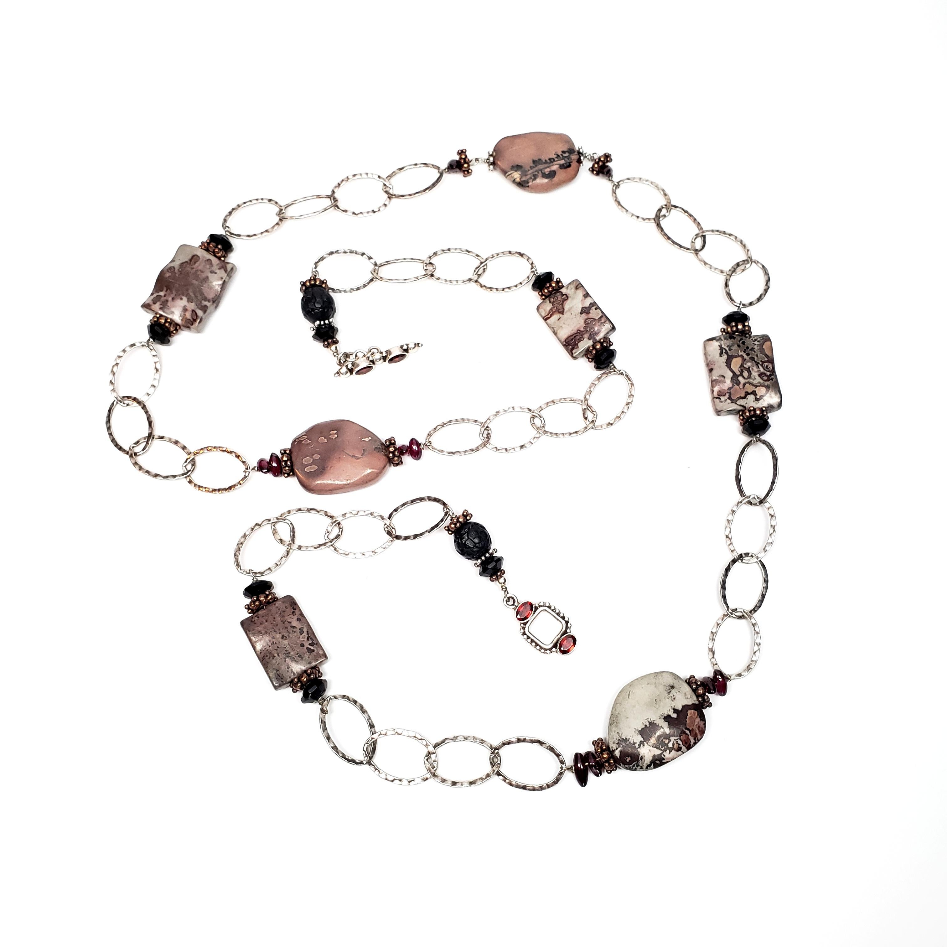 Sterling silver hammered oval link and stone necklace.

Chain features large hammered oval links with large veined cabochon stones. Each large stone is adorned on either side with a cluster bead and small stones. Toggle closure with deep red