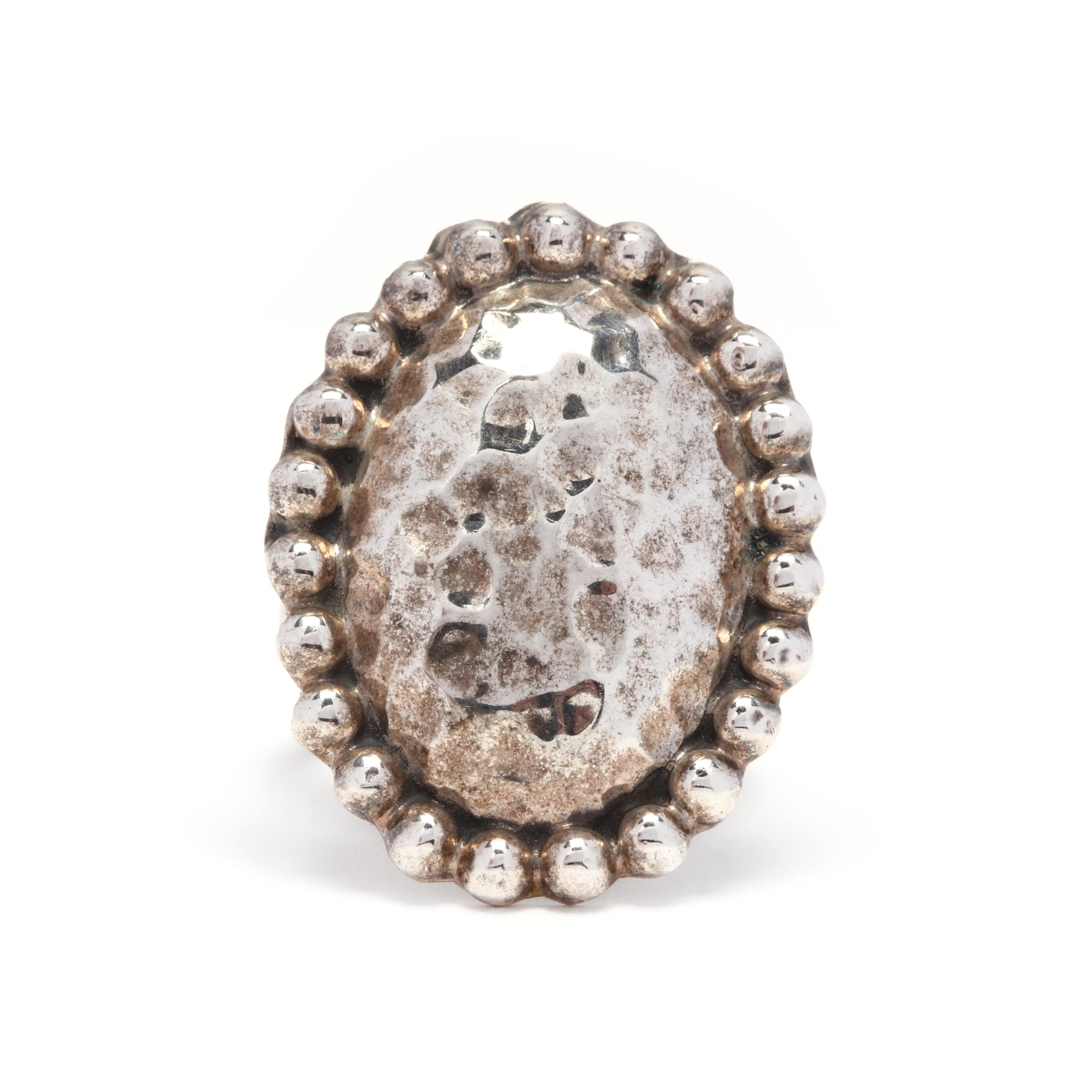 A sterling silver hammered oval statement ring. This ring features a large, hammered dome oval surrounded by a beaded halo and with a polished shank.

Ring Size 6

Length: 1 1/8 in.

Width: 7/8 in.

8.12 grams

* Please note that this is a vintage