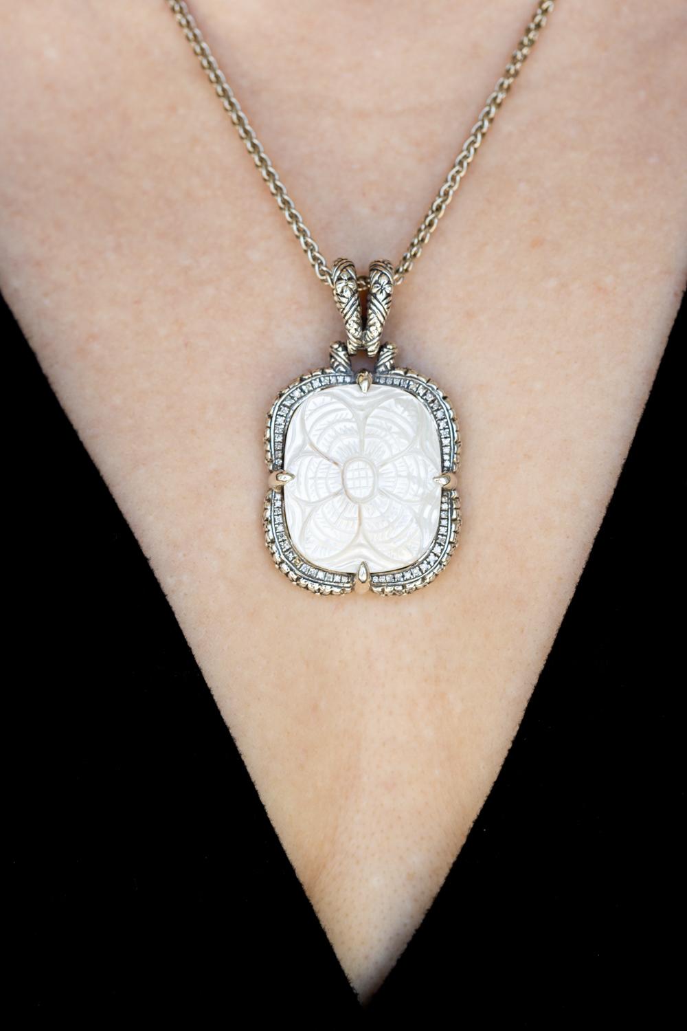The hand-carved mother-of-pearl pendant necklace by Stephen Dweck is an exquisite example of fine craftsmanship. Set in sterling silver, the pendant features intricate carvings on the lustrous mother of pearl, which is beautifully complemented by a