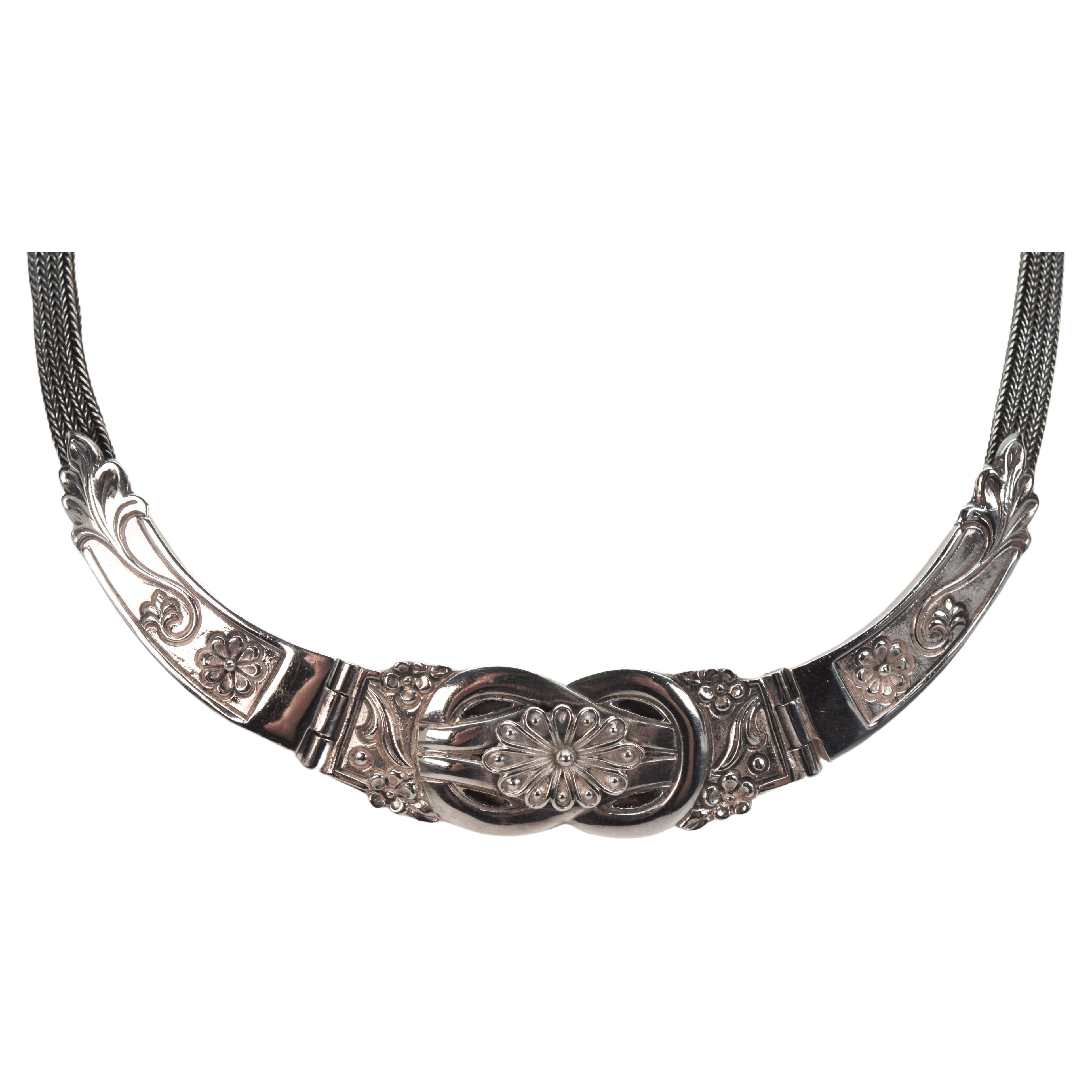 Three decorative floral hinged panels of die struck sterling silver create the front placket of this vintage collar necklace. Soft woven quarter inch mesh silver chain continues around the back of the neckline to the hook and eye closure that is