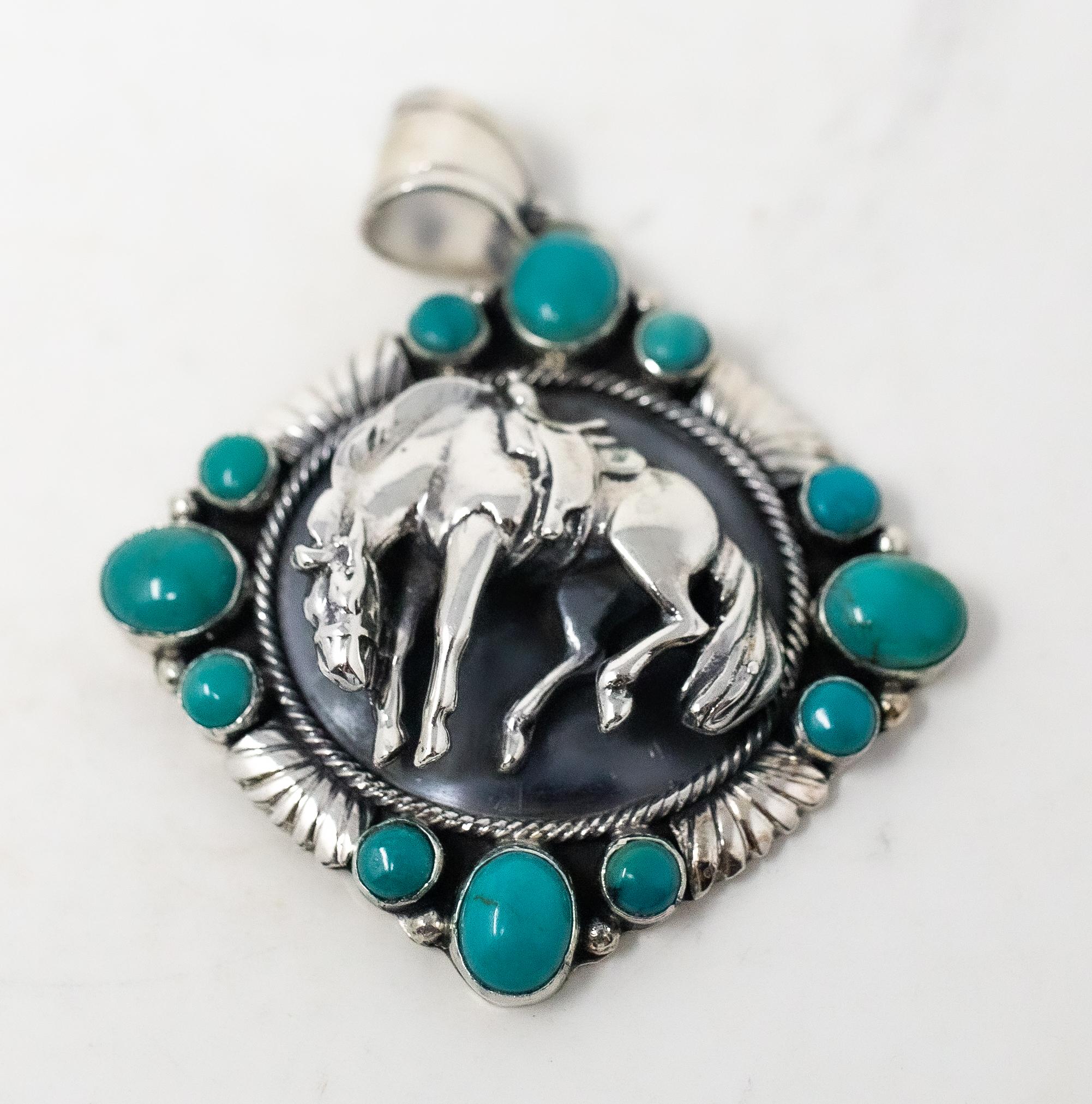 Offering this magnificent Navajo sterling silver horse pendant with turquoise by Emer Thompson. The sterling horse is bucking against a dark background surrounded by a spiral motif. The outer edge has four grouping of turquoise stones in sets of
