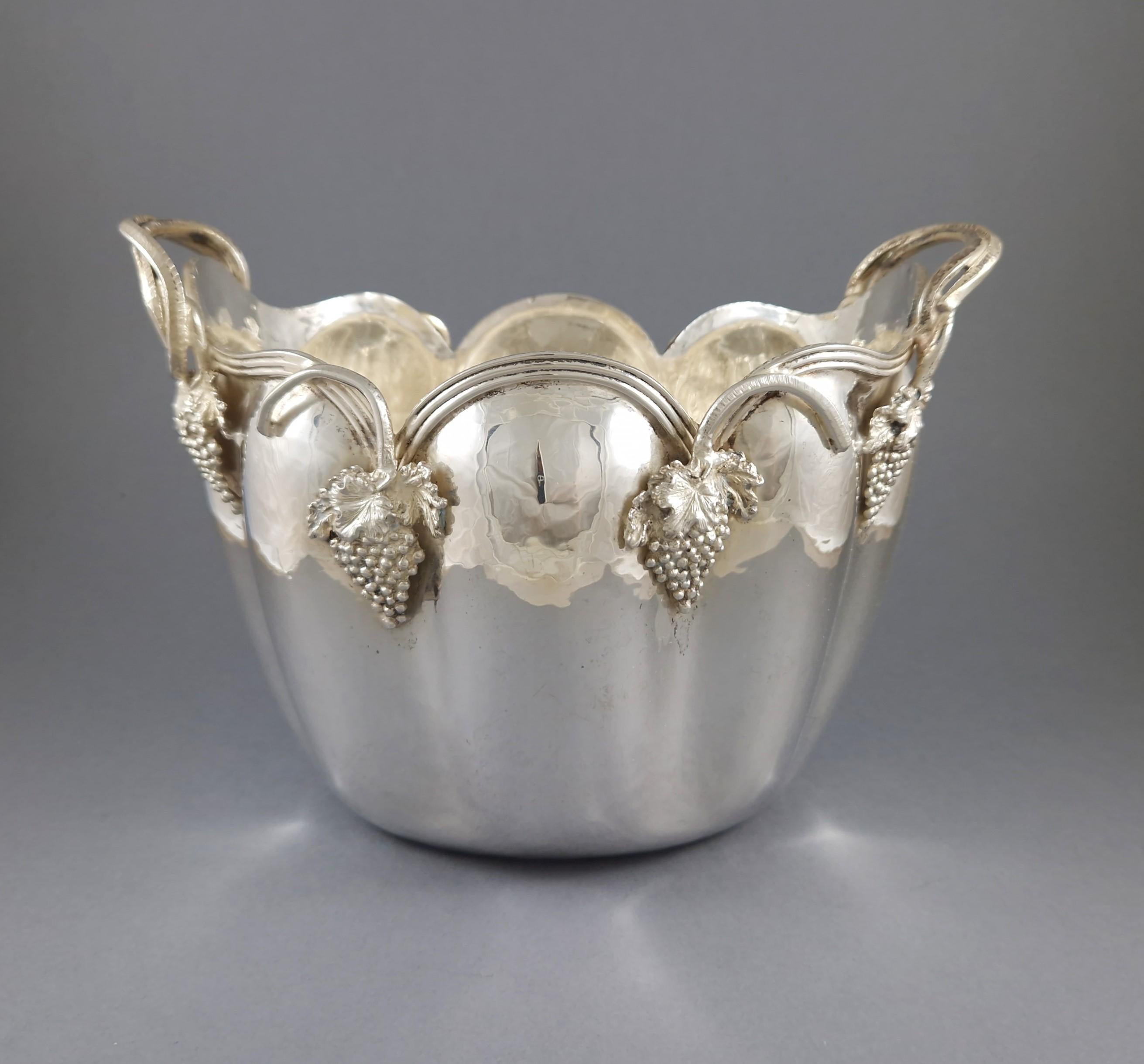 Secchiello per il ghiaccio in argento Sterling dalla forma arrotondata e lobata con bordo ondulato e smerlato, con bordi applicati a grappoli d'uva e foglie di vite finemente dettagliati e dotato di due manici ad anello a voluta. 
Un pezzo
